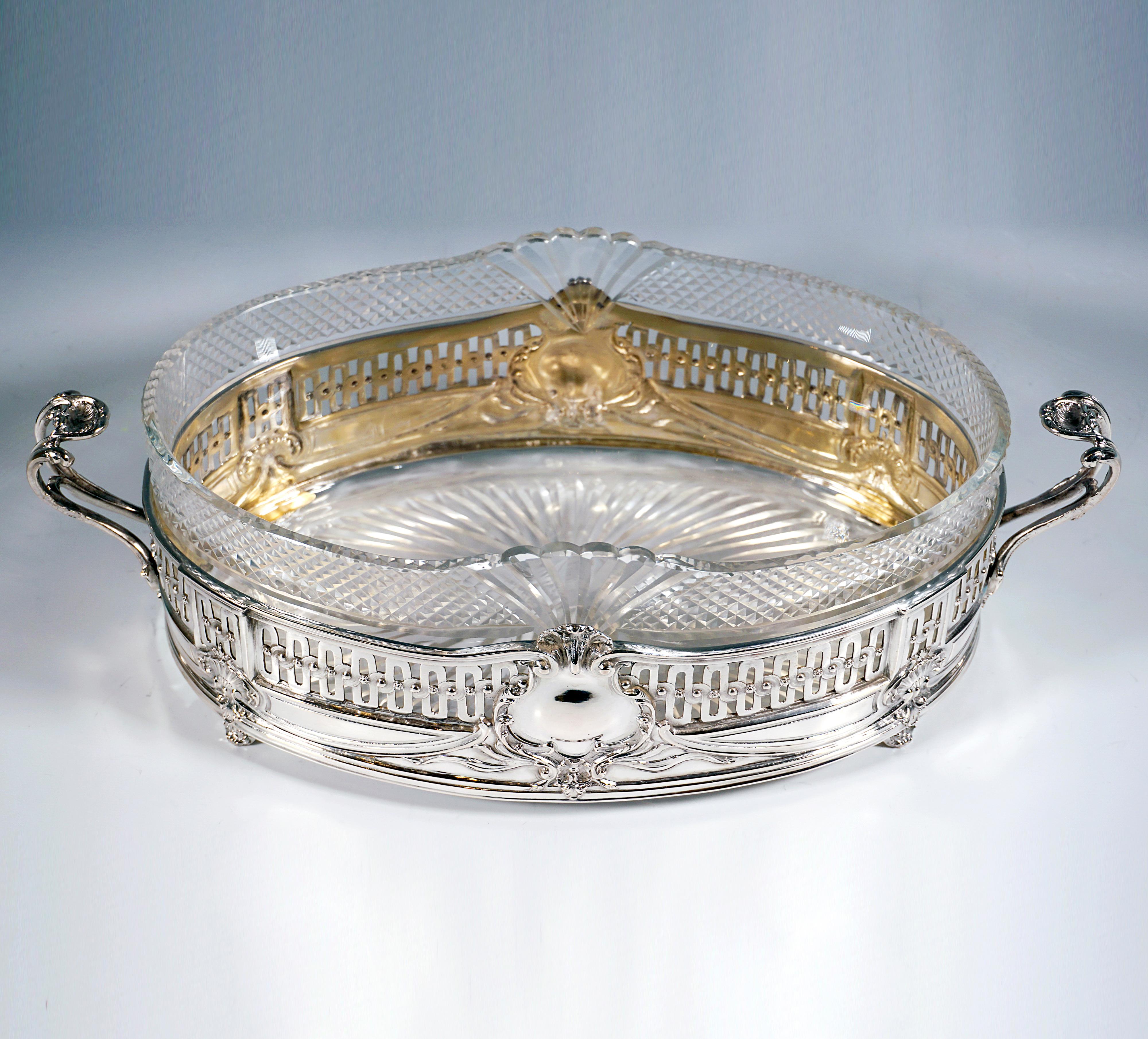Elegante jardinera de plata de forma básica elíptica sobre cuatro pies con decoración de rocaille, pared vertical recta con aberturas regulares en forma de bandas curvas en la zona superior, debajo bandas curvas en relieve con elementos de rocaille