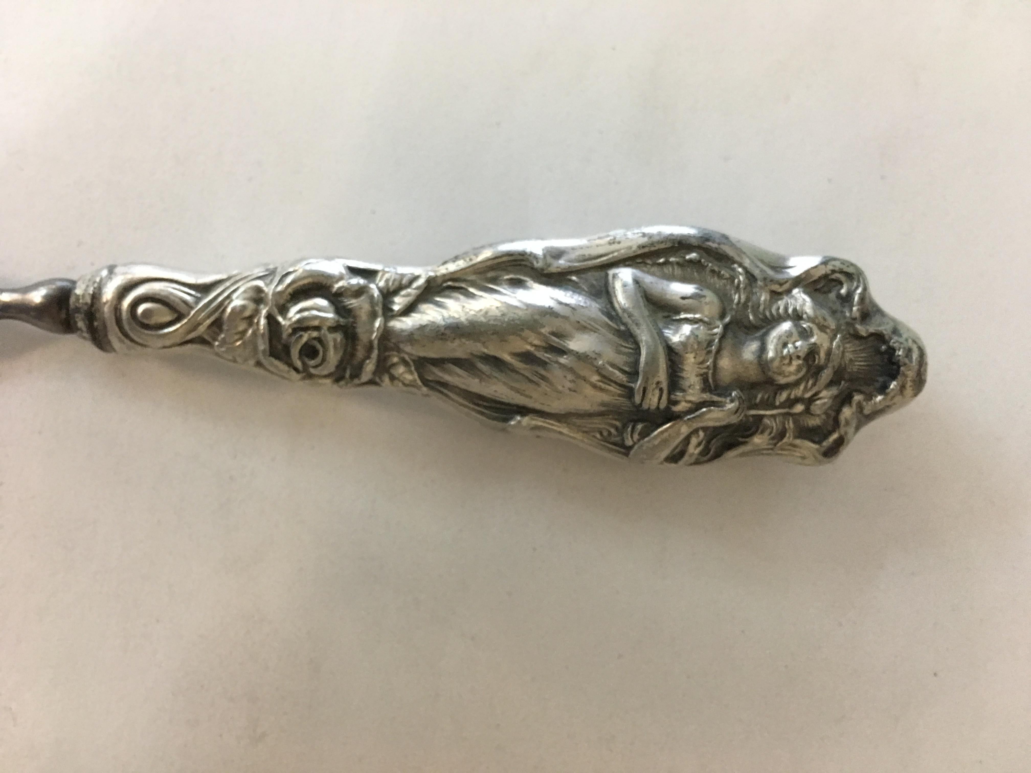 This piece is a silver plate nail file with Art Nouveau designs along the front. The handle features a relief of a woman holding a flower in great detail, circa 1900.