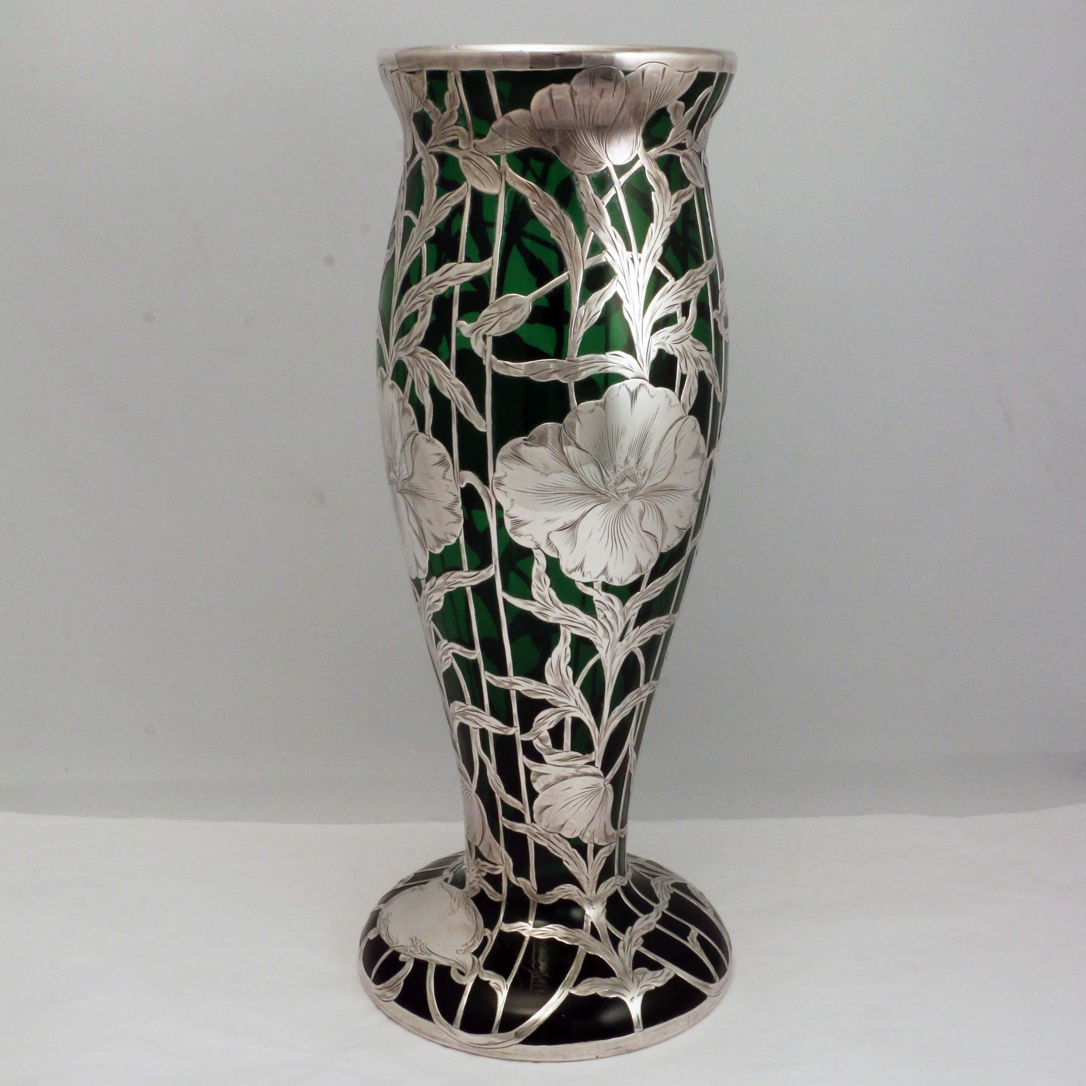  An American specialty often by the Alvin  Co. to whom we attribute this.;the vase is very large  and with gently swelling baluster. .On a deep emerald-green ground , the silver overlay climbs with leaves and tendrils and with soft poppylike