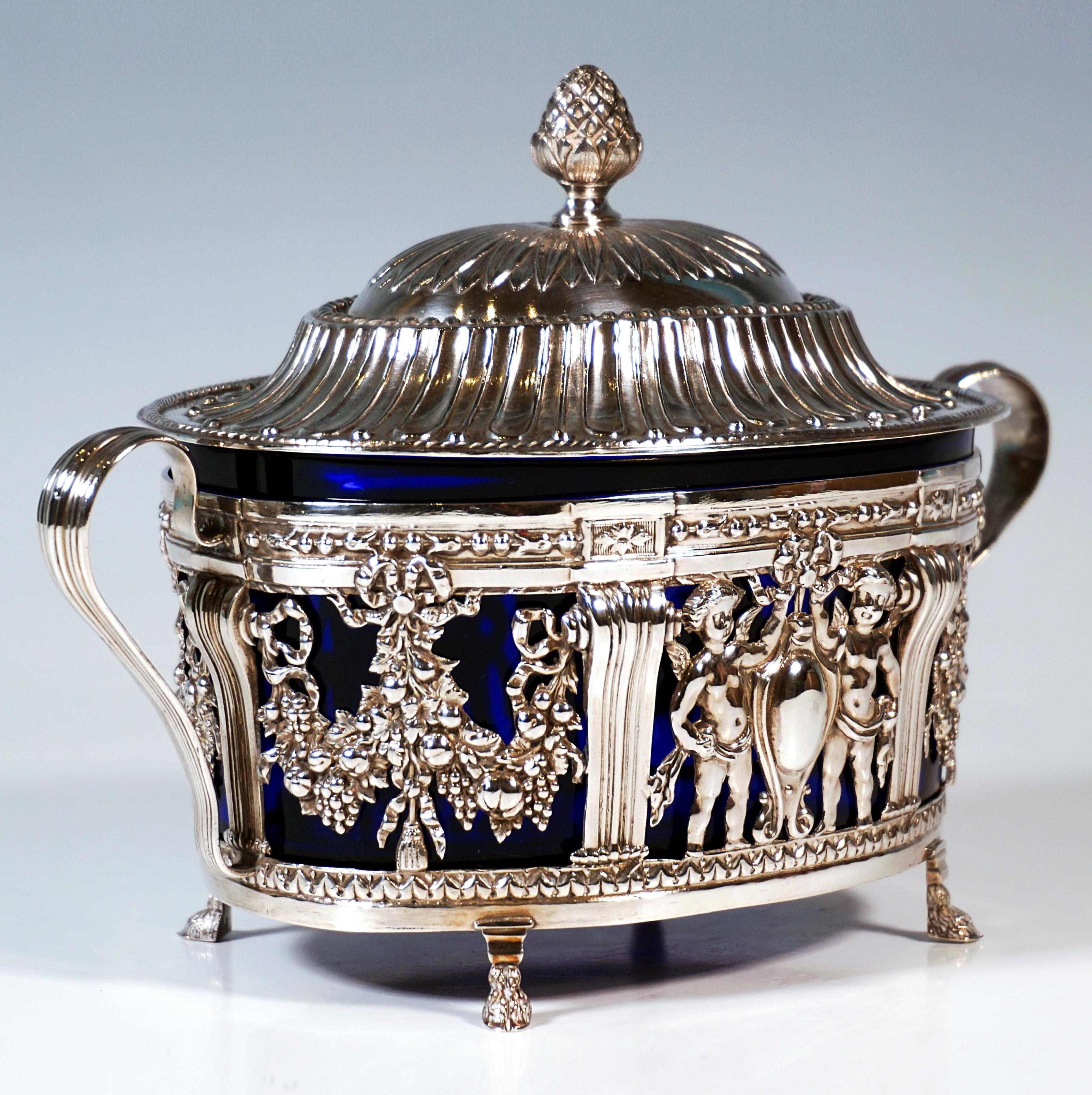 Élégant sucrier en argent de forme ovale, reposant sur quatre pieds en forme d'animaux, corps droit légèrement évasé vers le haut avec un décor ajouré en relief, divisé en six segments par des pilastres, deux putti flanquent un cartouche décoré d'un