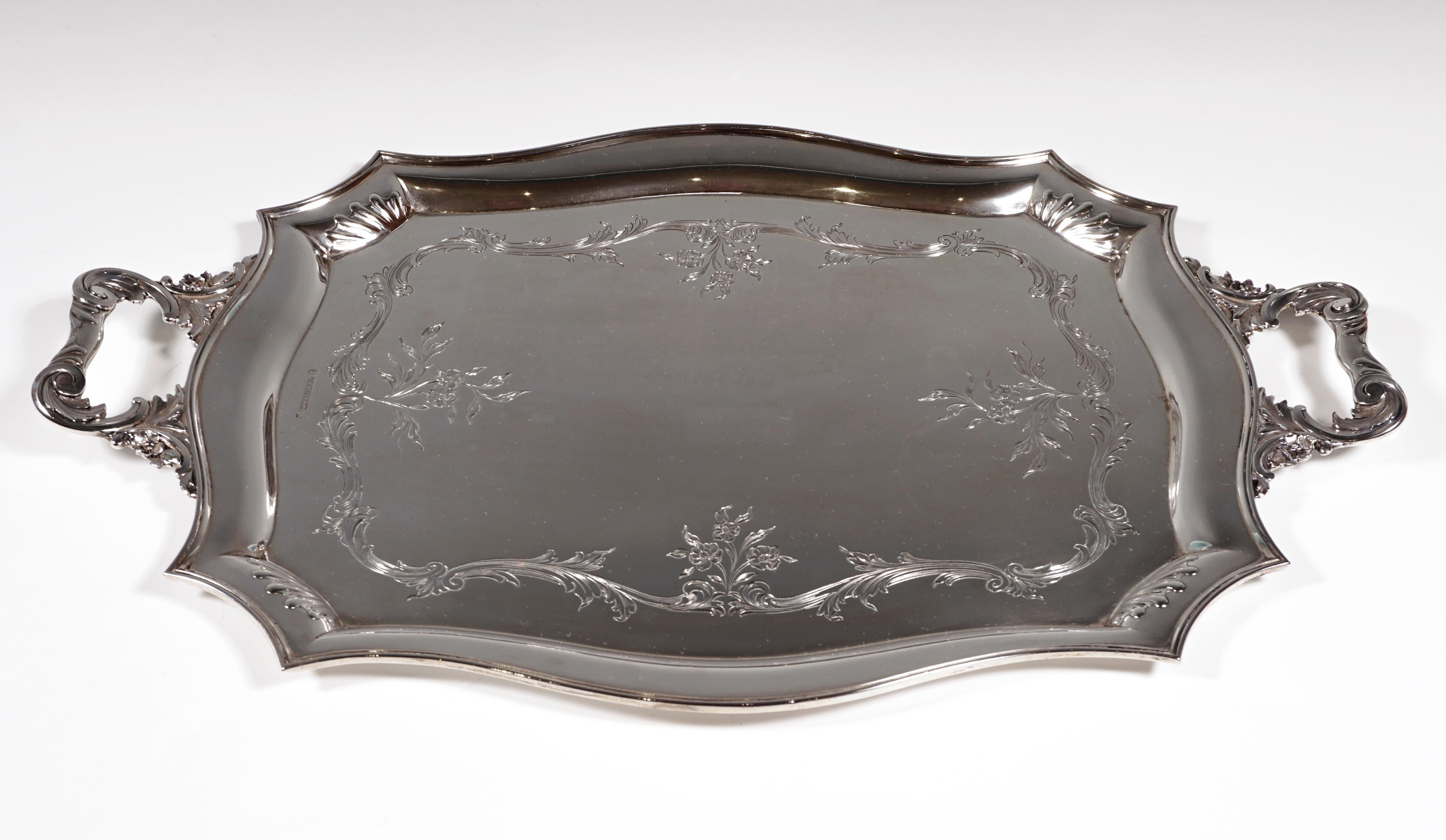 Silver tray in a rectangular basic shape with bevelled corners, accentuated by embossed hump decoration and curved, profiled edges, on the mirror, encircling volute and flower band, two volute handles with floral decoration on the short