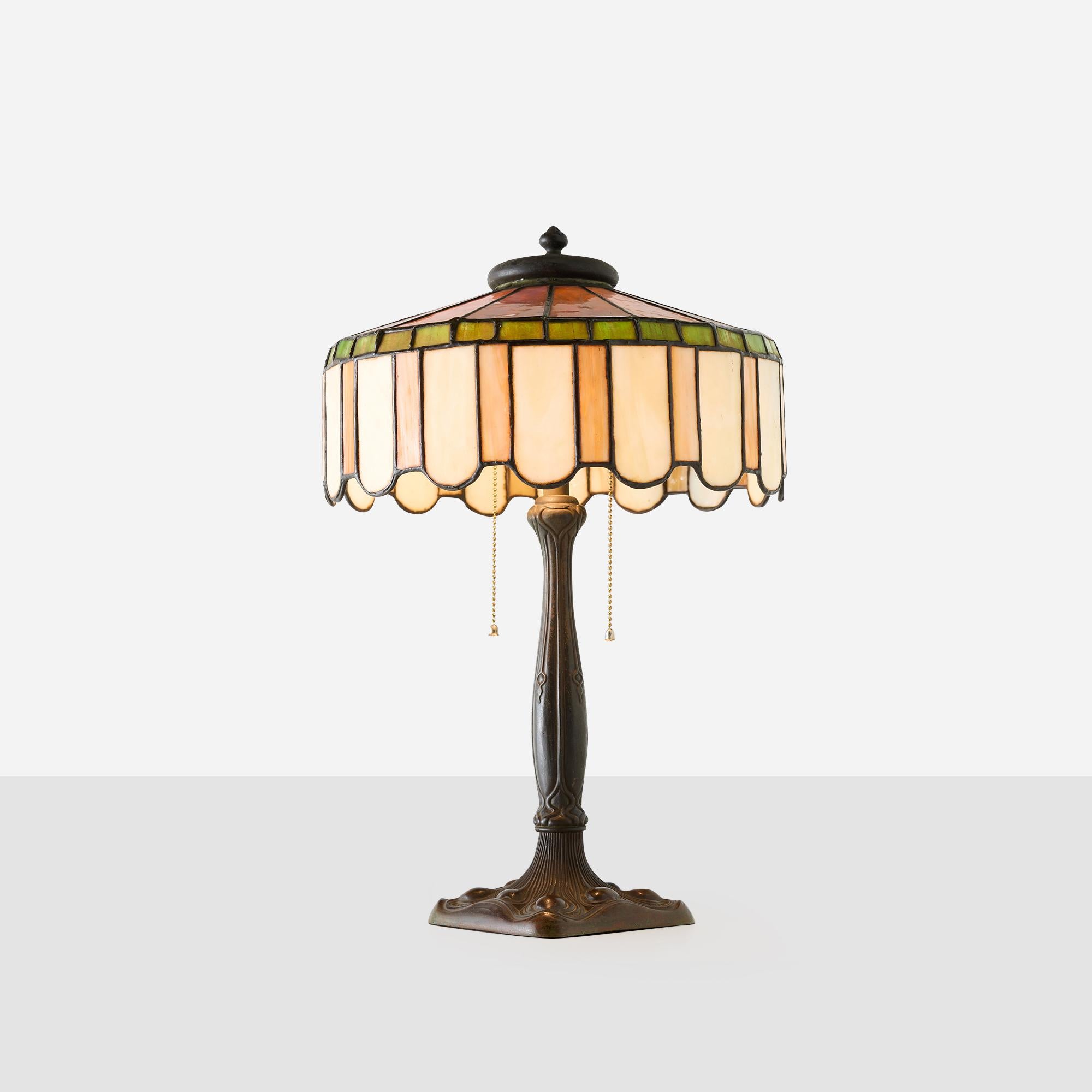 Lampe de table américaine en verre de scories de style Art Nouveau, probablement des années 1910 à 1920. L'abat-jour en verre vert, ambre et crème est recouvert d'un métal décoratif. La base est en métal moulé avec une patine chaude.

Non marqué,