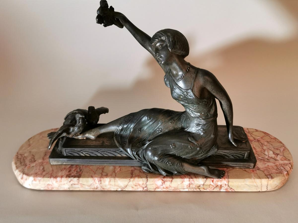 Particular antimony statue depicting a girl sitting in a sweet and elegant way; in his raised right hand he holds a rose in a symbolic offering; at his feet, two doves seem to coo between them; the girl's clothing and hairstyle are typically