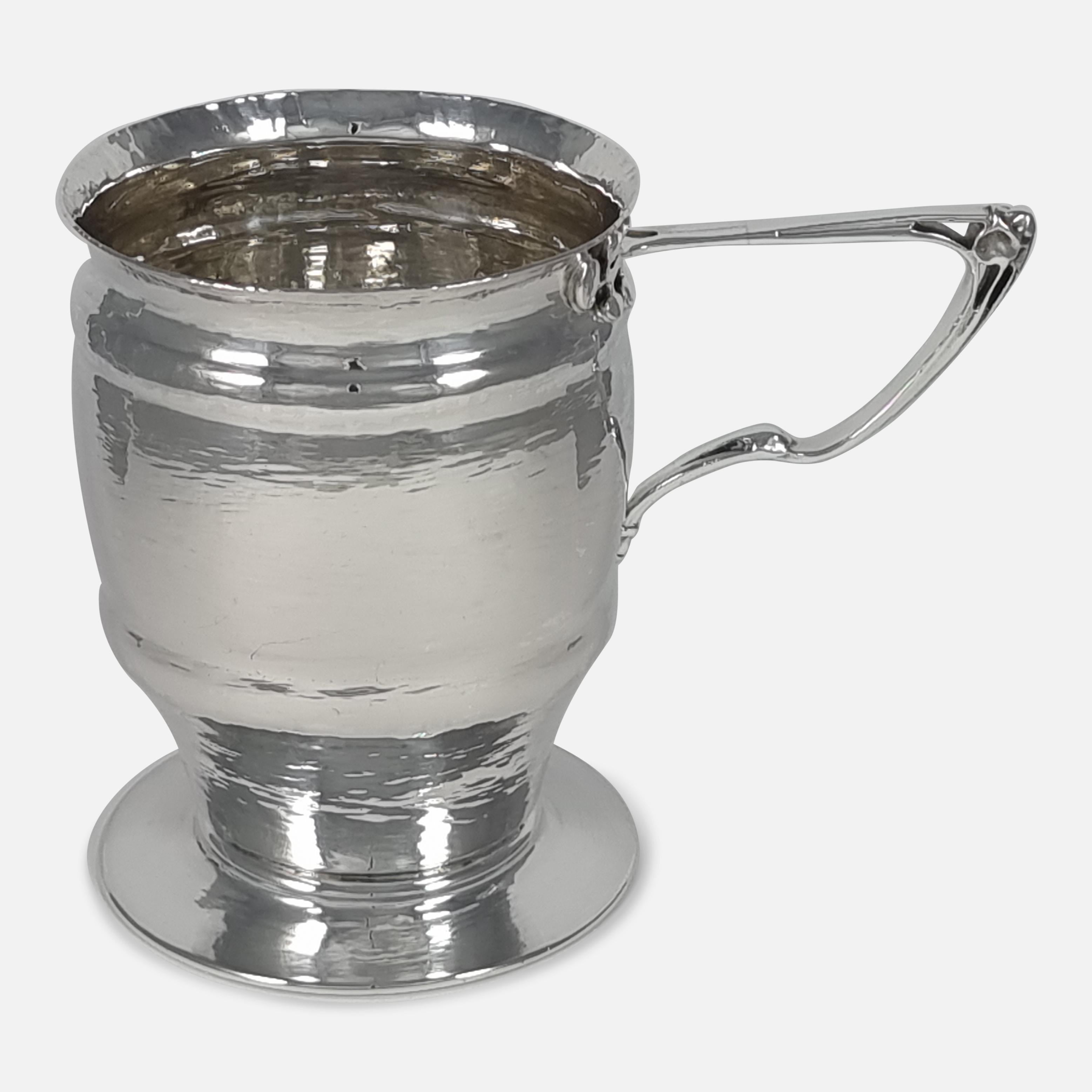 An Edwardian sterling silver mug in the Art Nouveau style. The mug is of planished and double ogee banded beaker form, with a spreading foot, the bisecting pierced handle is of an naturalistic whiplash design.

Assay: - .925 (Sterling