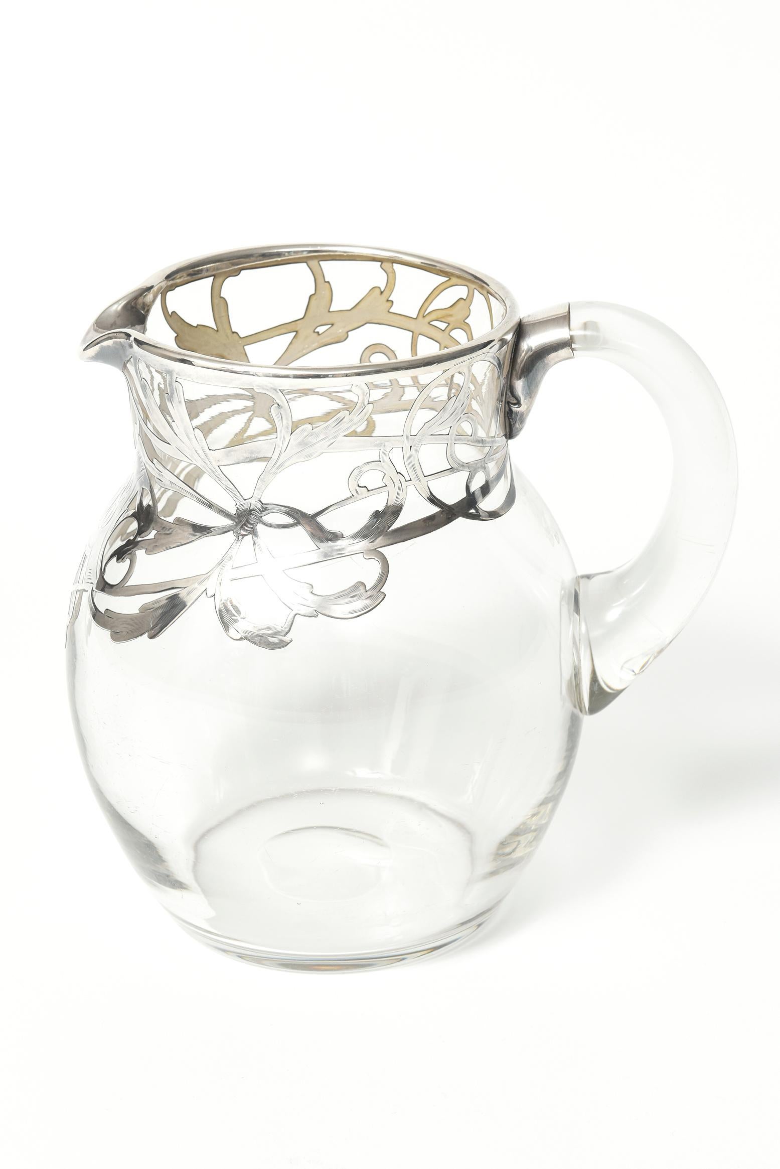 Beautifully made Art Nouveau water or lemonade pitcher with a sterling silver flowing vine design. The area below the spout has a plaque with initials. Initials say SJG or LJG.

No marks on the pitcher.