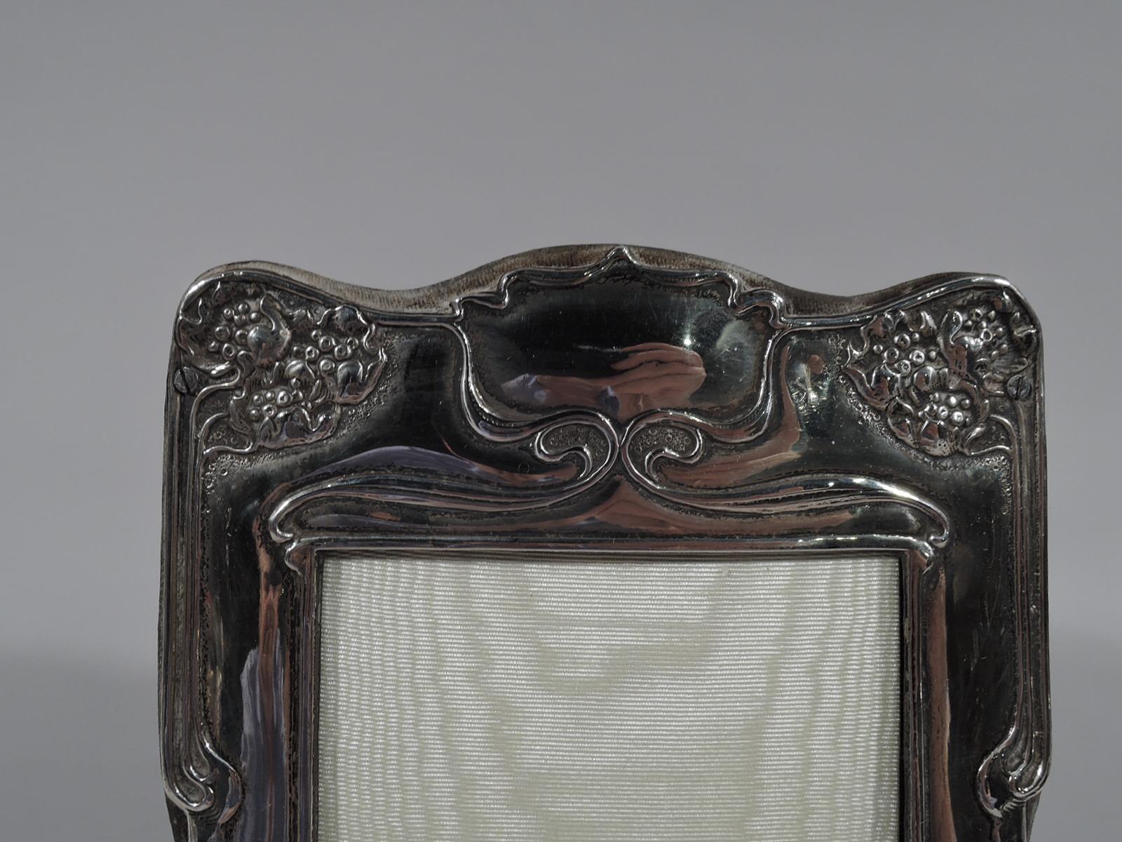 Turn-of-the-century Art Nouveau sterling silver picture frame. Made by Dominick & Haff in New York. Rectangular window in shaped surround with bracket feet. In English Liberty style with raised symmetrical ornament with whiplash lines, tendrils, and