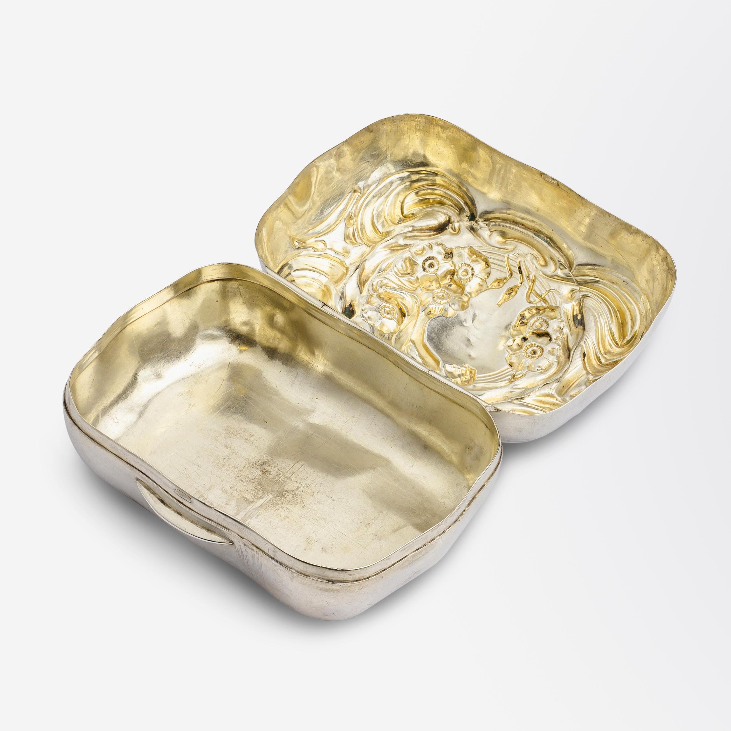 This vanity box was created around the Turn of The Century by American firm, Unger Brothers. The hinged box features a lid with heavy repousse detailing depicting a reclining female amongst flowers and bold Art Nouveau swirls. The box was likely