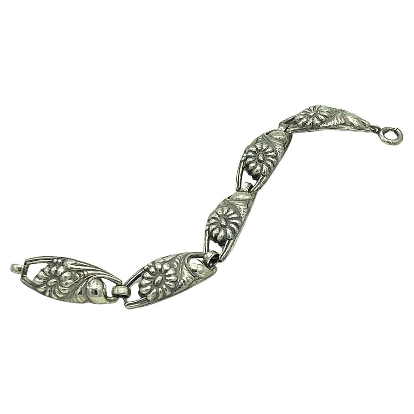 This is a 1930s Art Nouveau style sterling silver bracelet. It has five deeply embossed flower linked sections and a spring ring clasp.  Marked 
