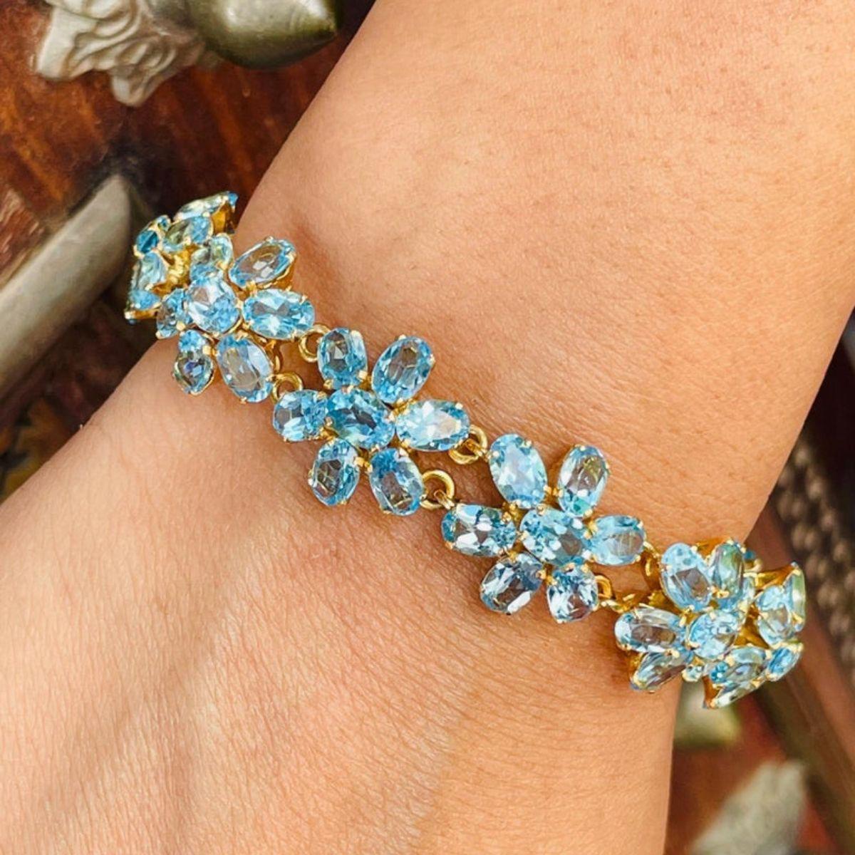 This Blue Topaz Flower Bracelet in 18K gold showcases 77 endlessly sparkling natural blue topaz, weighing 38.1 carats. It measures 7.5 inches long in length. 
Blue topaz helps to improve communication and self expression. 
Designed with perfect