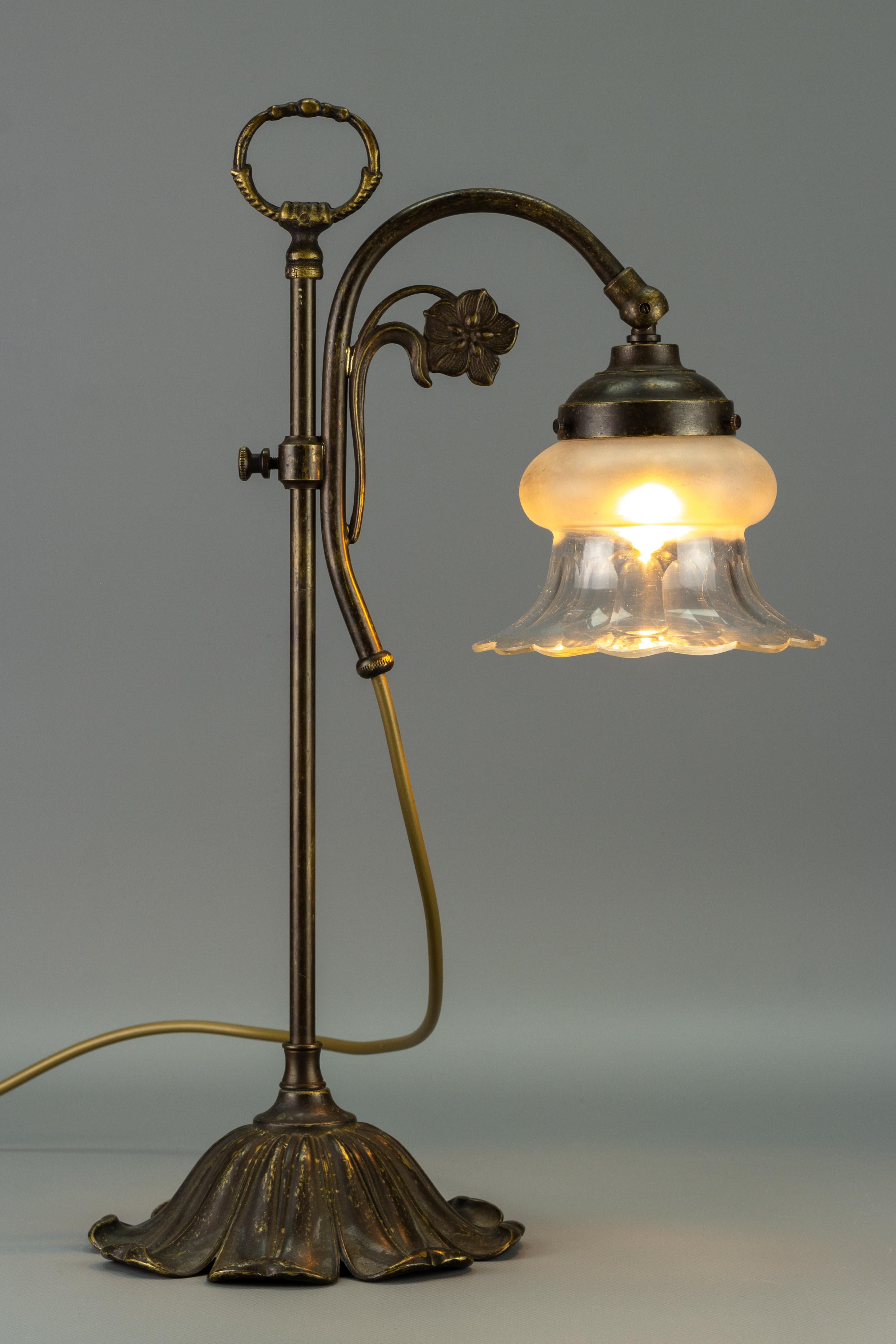 An adorable Art Nouveau-style vintage table lamp made of brass and metal, adorned with floral decor. The base is in the shape of flower petals; the glass shade is partially frosted and translucent. The height of this beautiful table lamp is