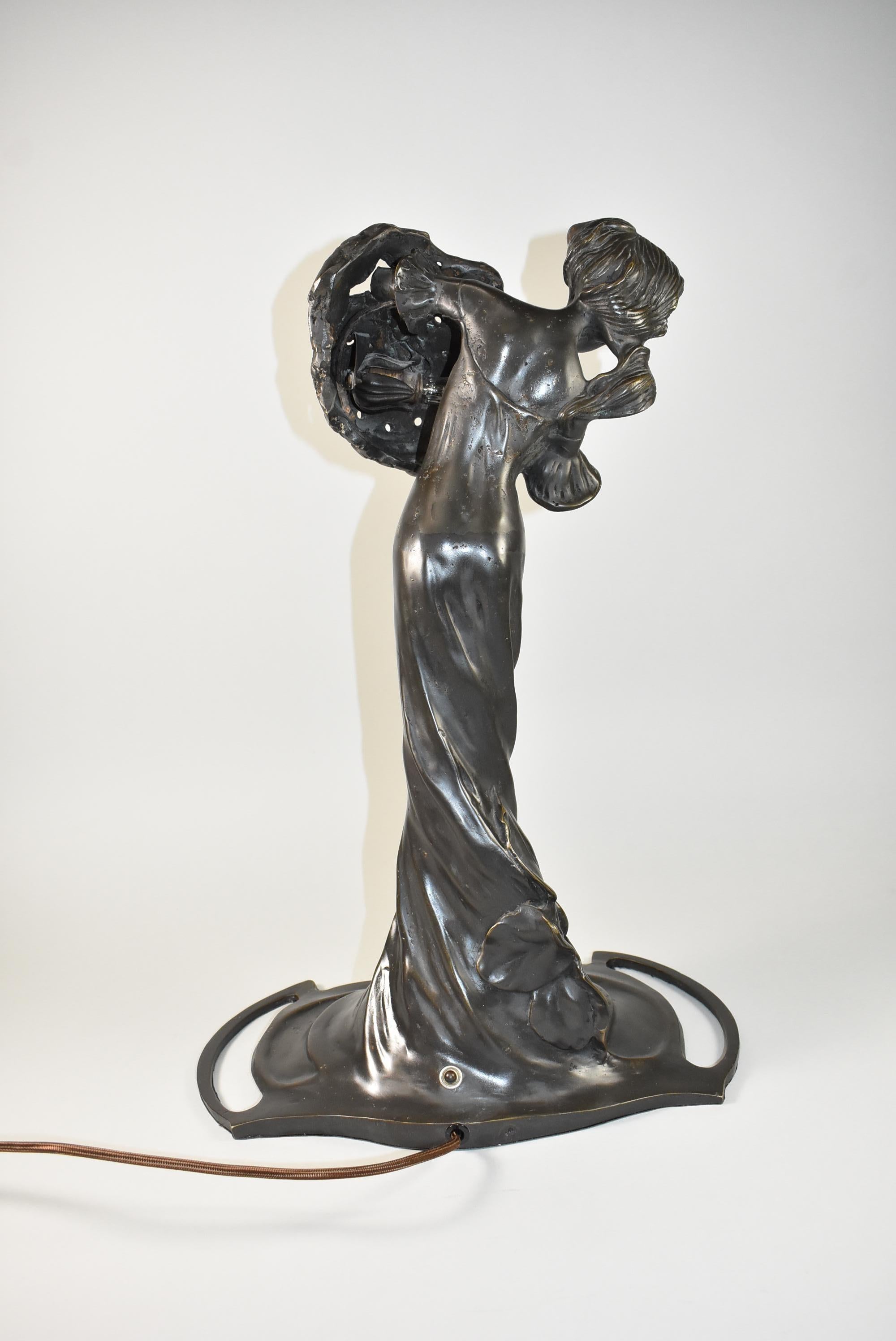 Cette belle lampe sculpturale représentant une femme avec des fleurs est dans le style Art Nouveau. Les fleurs sont percées avec la douille derrière pour laisser passer une douce lumière. Sa robe tourbillonne autour d'elle pour la base. Cette pièce