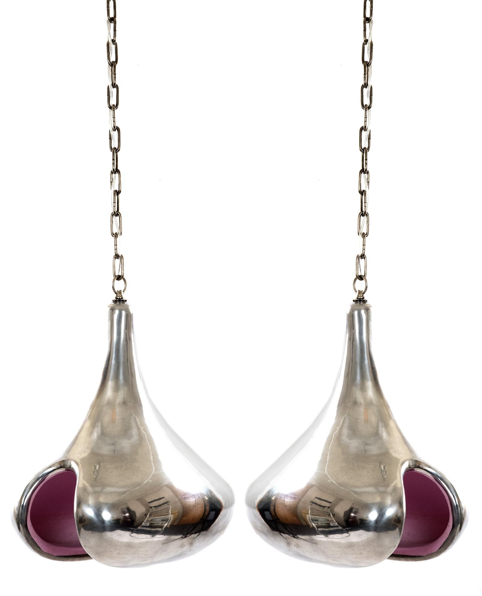 A pair of Art Moderne cast aluminum pendant lights of tear drop form, the silhouette having an open central space with a juxtaposing pink interior, with a chain suspension. Measures: 21 x 13 x 17 inches (not including the chain).