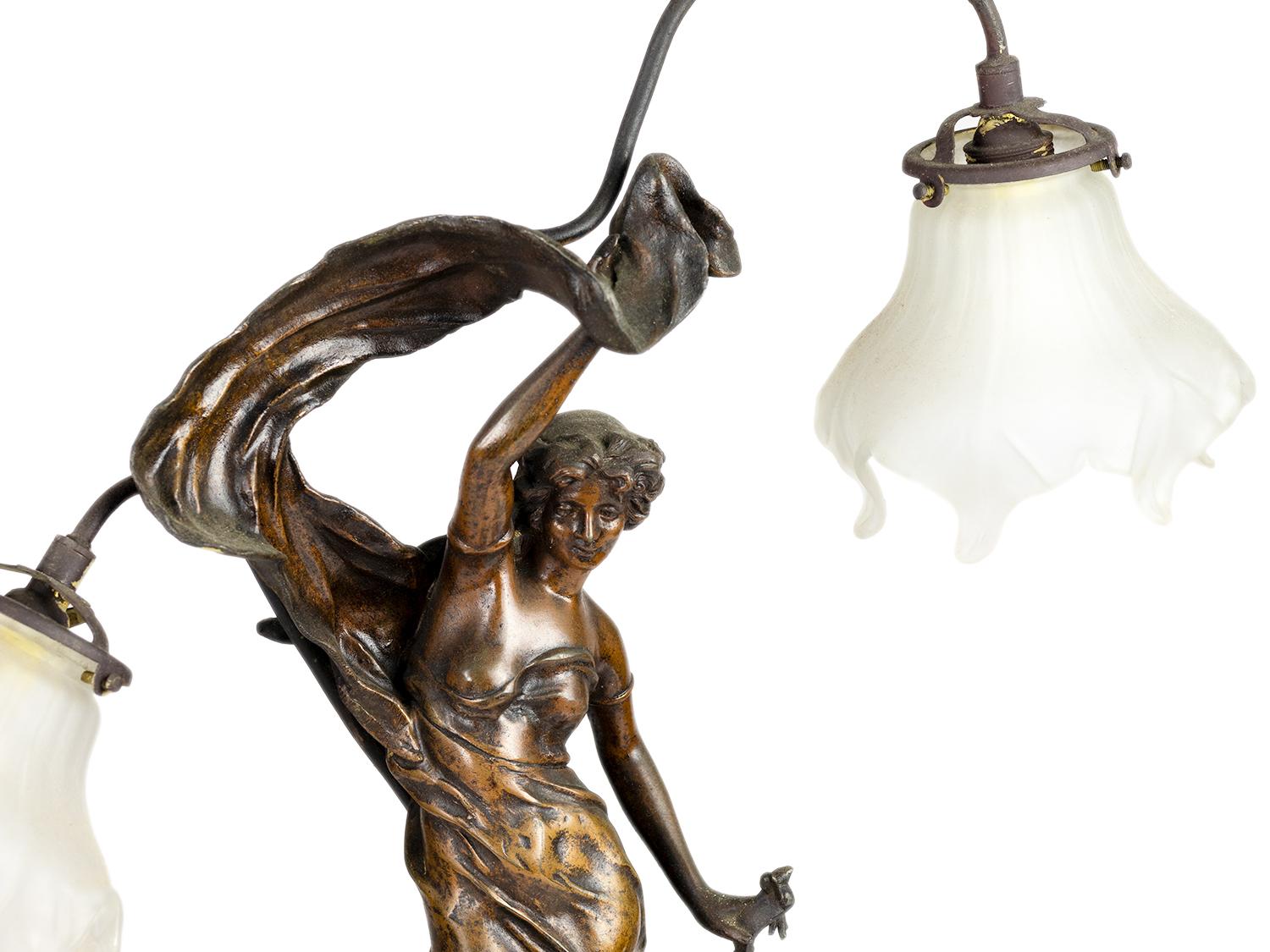 A table lamp from 1889 in spelter with two illuminated tulips and a model
of the sculpture 'Lever de l'aurore' - The Dawn in spelter, two arms and opaque pearl white tulips. 
Front plaque 'Lever de l'aurore par J. Causse'. 

Jules Caussé, son of the