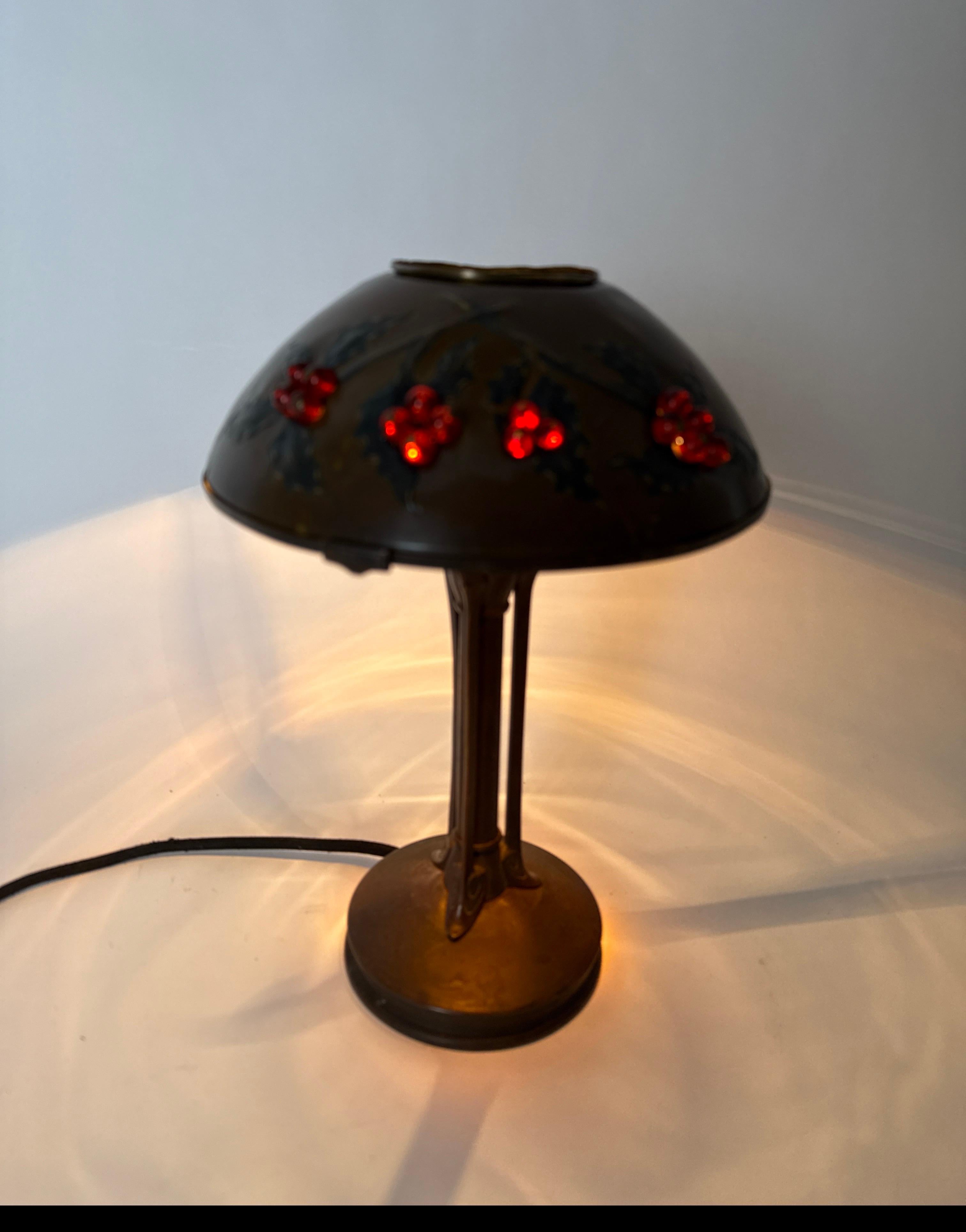 This small table lamp is a small work of art. The beautiful Jugendstil lamp base is designed in the classic style of the heyday of this style era. The lampshade is a brass lamp dome that is open at the top, the sides are decorated with raised holly