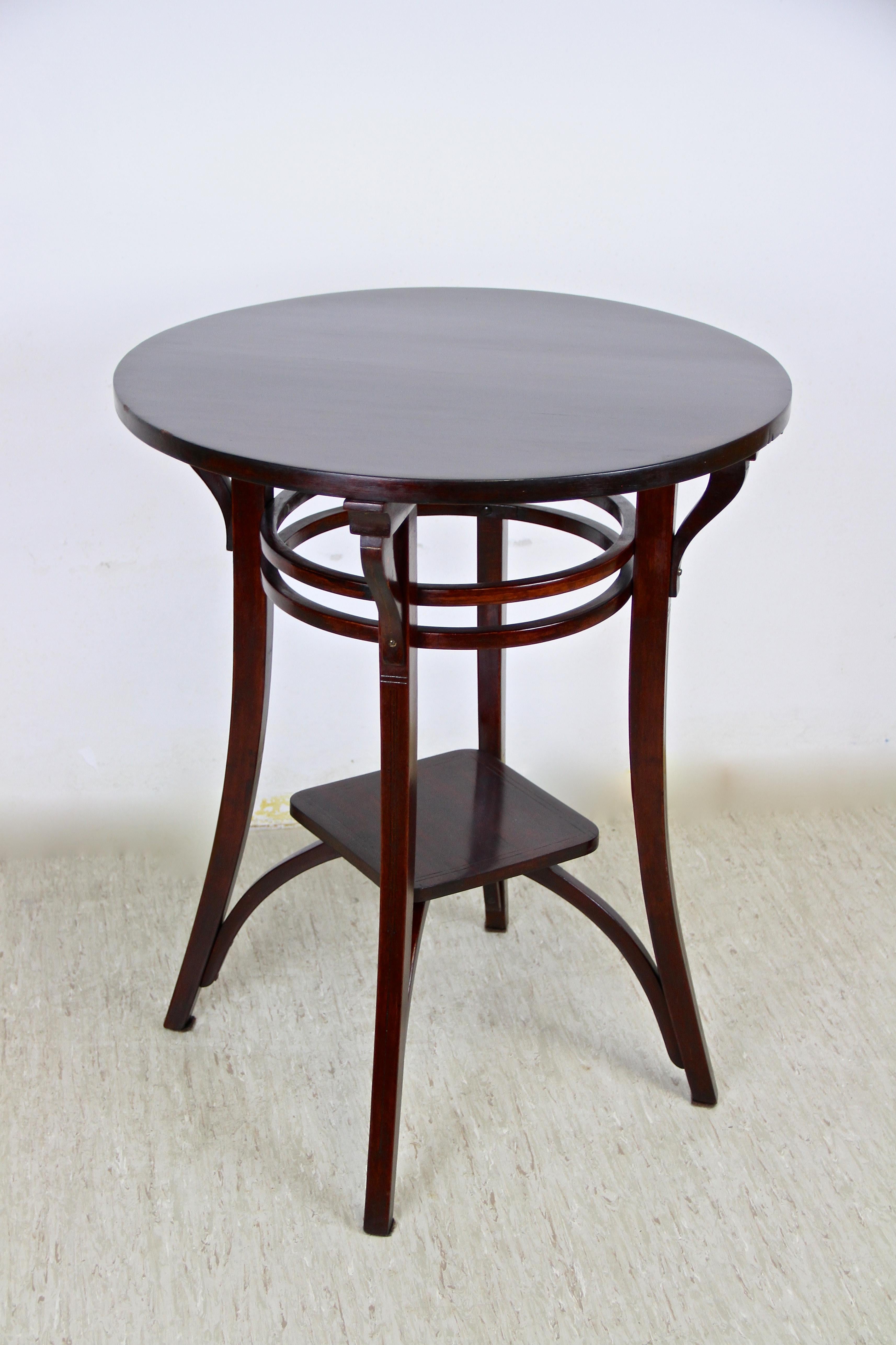 Timeless bentwood side table by the famous company of Thonet Vienna/ Austria from the early 20th century, circa 1905. The round table impresses with an exceptional design and shows an additional compartment in the lower third which floats on four