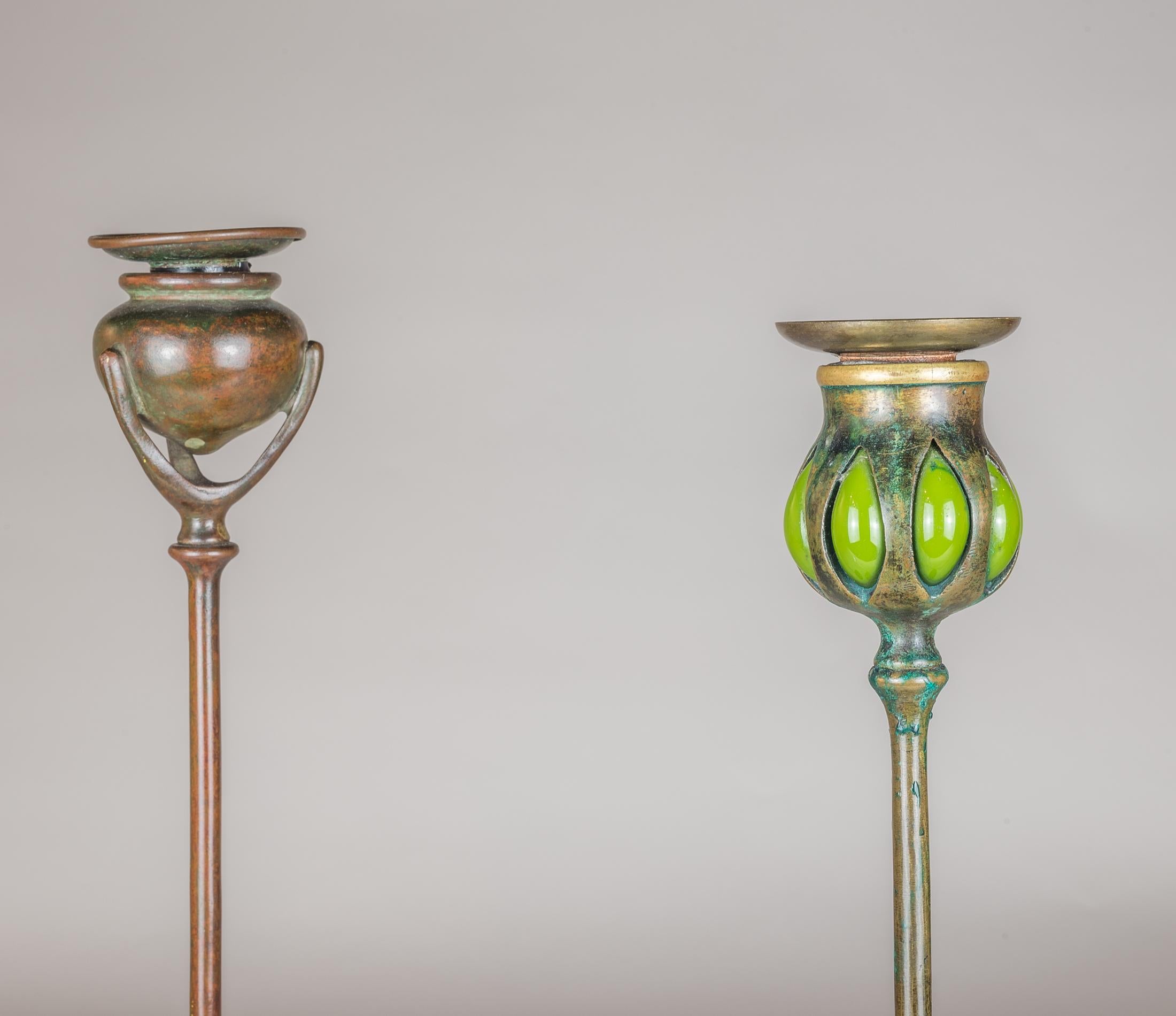 Two American patinated-bronze art nouveau candlesticks by Tiffany Studios in New York. One stamped 1213, the other mounted with green glass to look like a budding flower about to burst, stamped ‘Tiffany Glass and Decorating Co. monogram and D419.