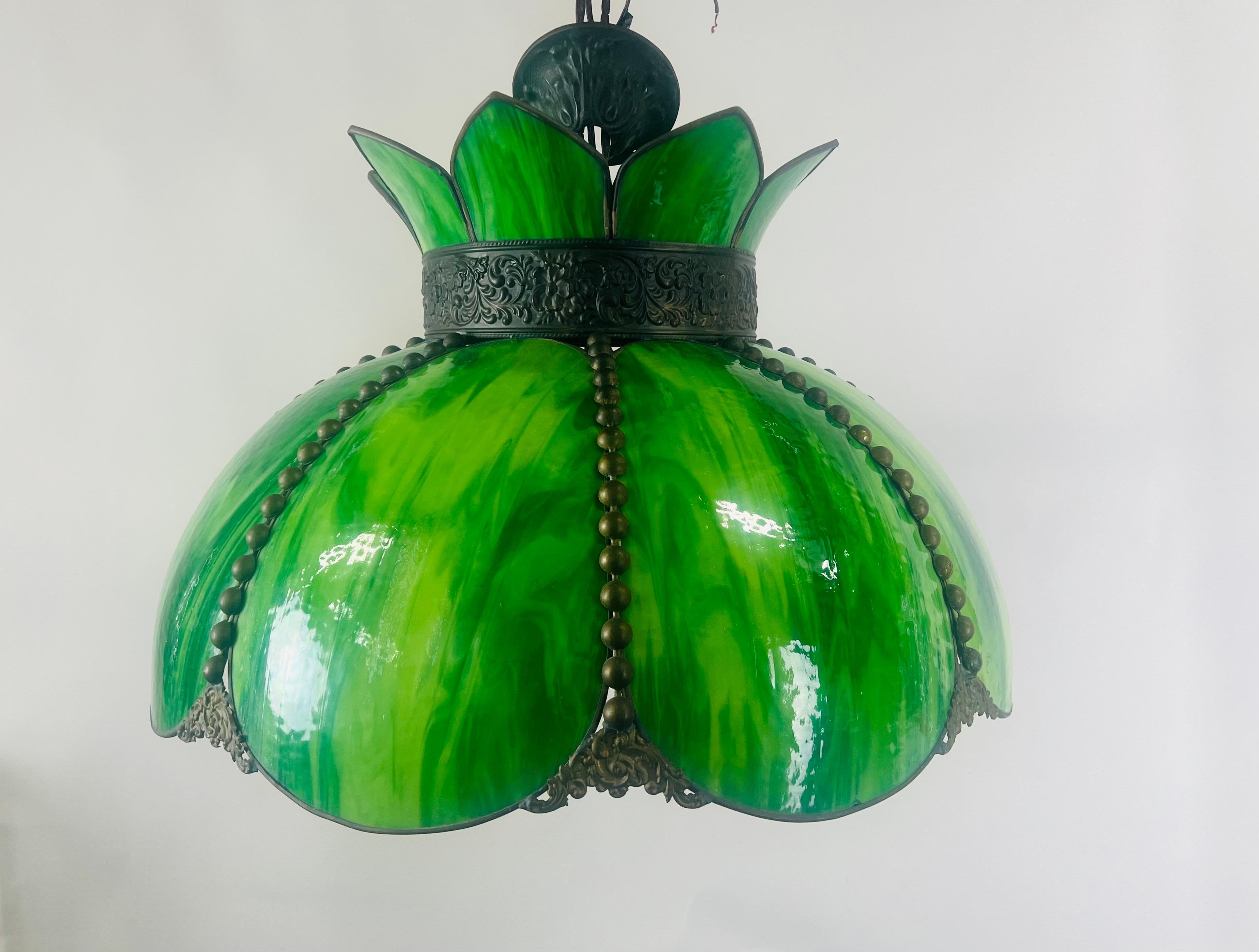 Ce lustre exquis de style Art nouveau Tiffany capture l'essence de l'artisanat du début du 20e siècle, mêlant forme organique et art vibrant. Les panneaux de vitrail vert luxuriant de la suspension rayonnent d'une profondeur envoûtante, évoquant les