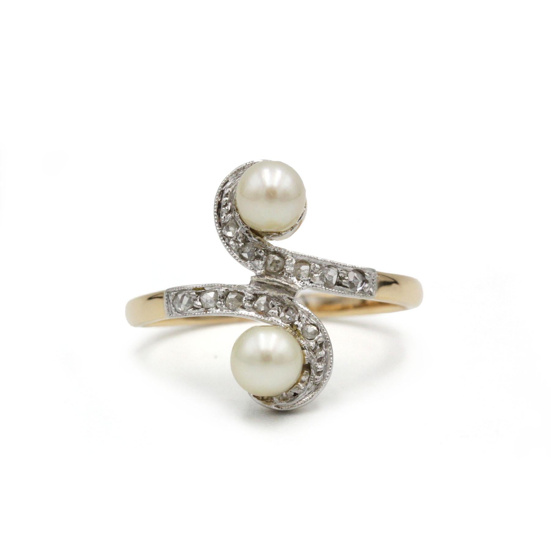This elegant Art Nouveau toi et moi ring features two natural pearls gracefully opposed in a flowing open design, symbolizing union and harmony. The curved platinum-topped setting is delicately pavé-set with glittering rose-cut diamonds, enhancing