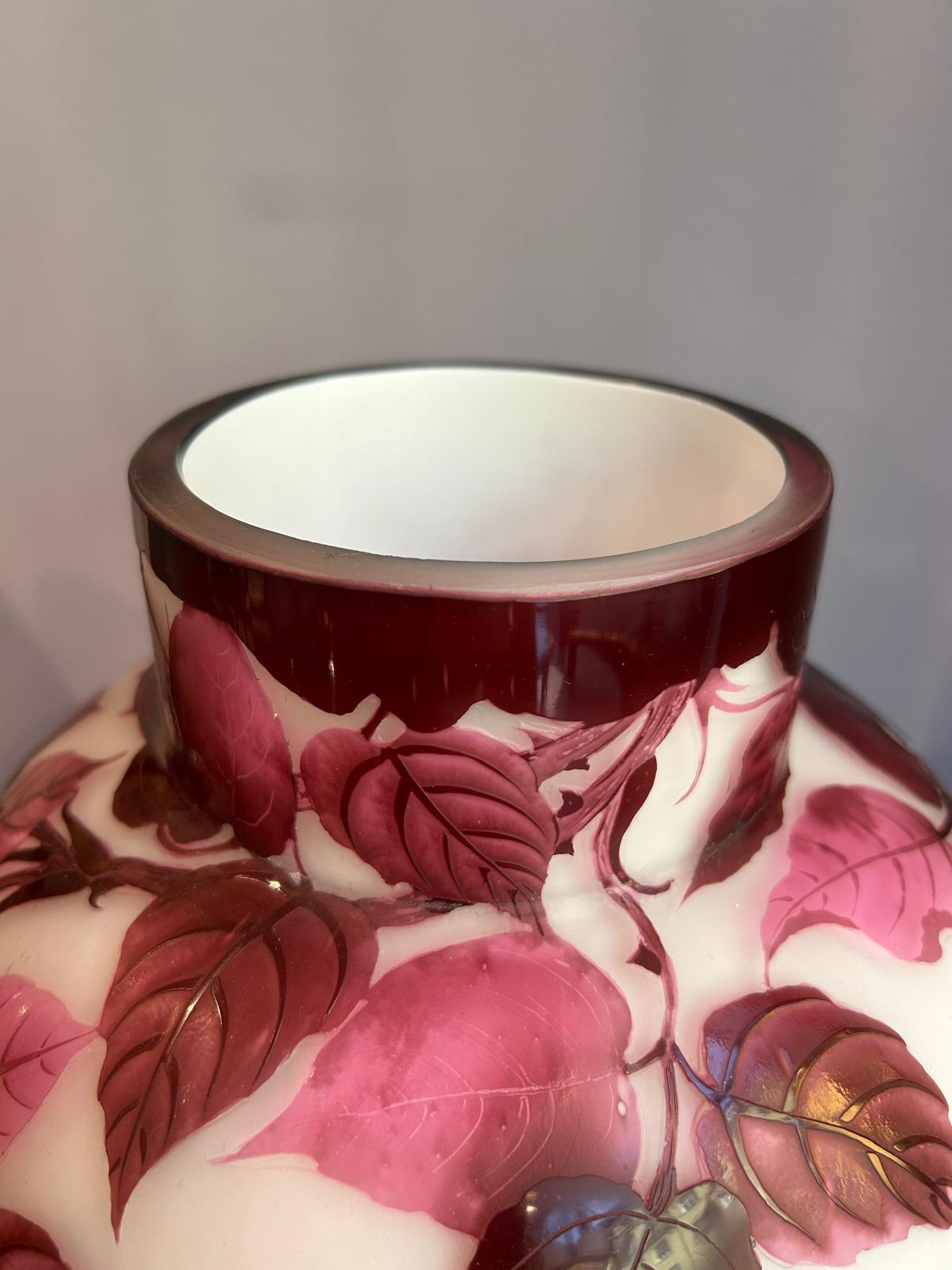 The vase by Loetz from around 1910, features white glass with a red overlay and is intricately etched with a rose motif. The leafs of the rose stand out in light pinkish to deep purple colors. The hight of the vase is 36.5 cm and it is a notable