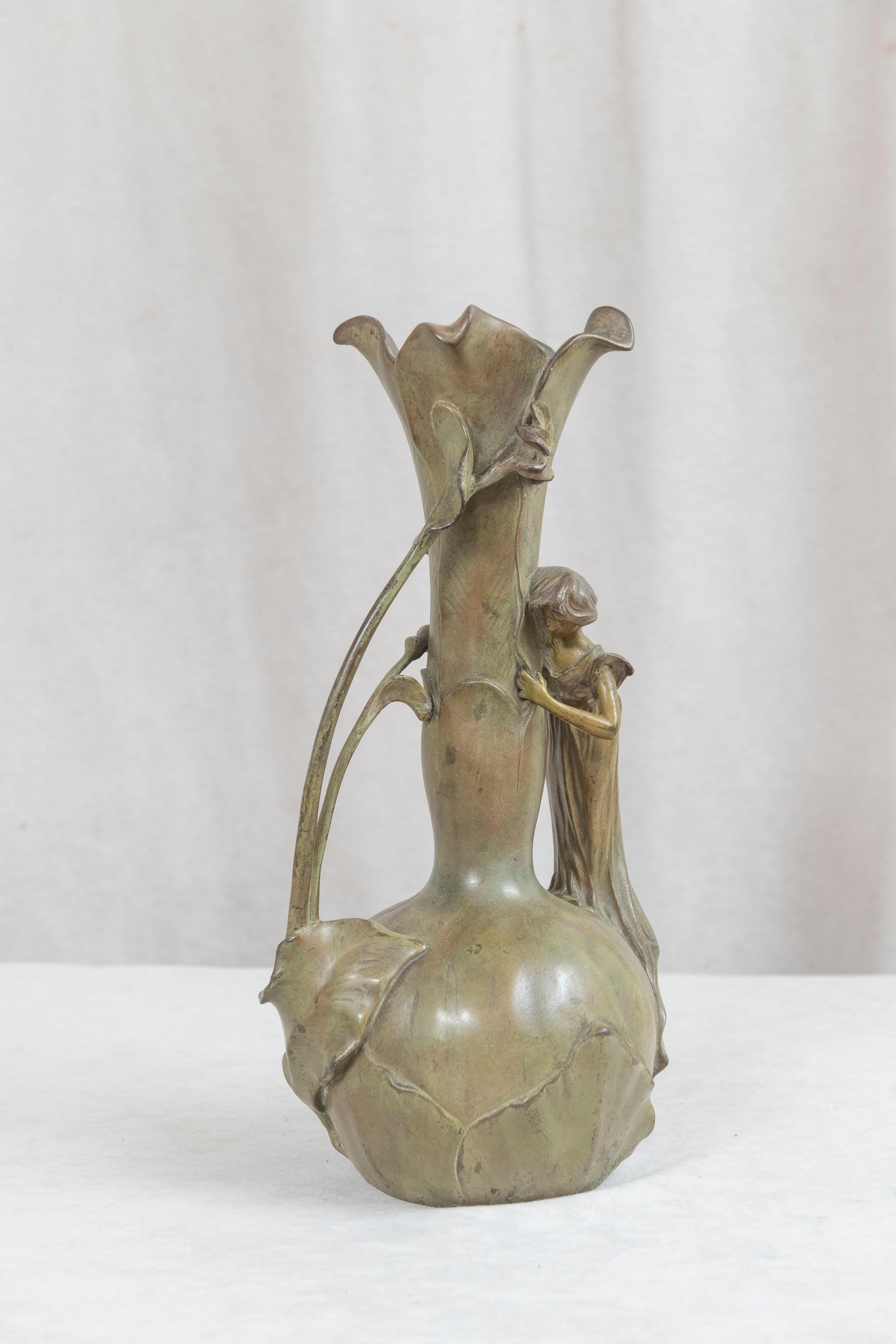 This lovely vase is a very fine example of the art nouveau style, and period. It has all the desirable elements needed to exemplify good art nouveau, sinewy lines, flowers, and the pretty girl embracing the vase. Done in an organic green patina and