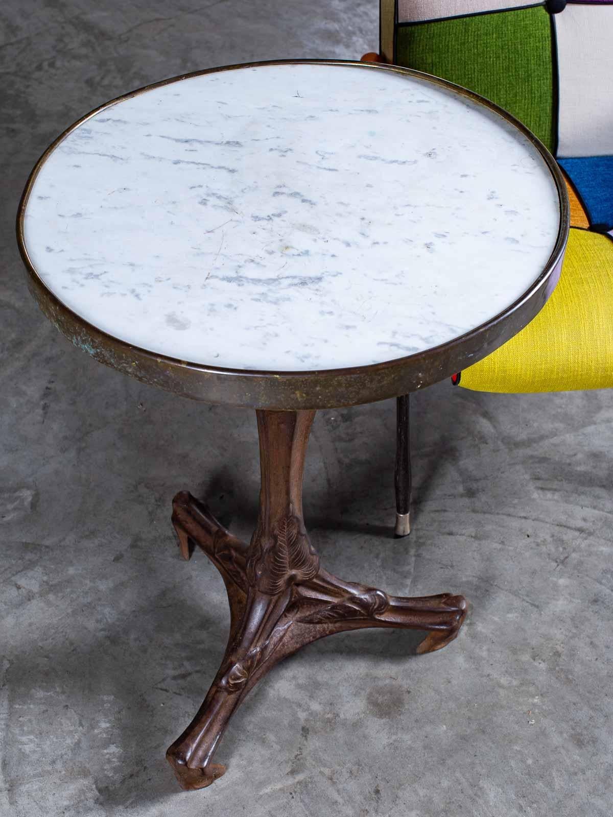 This handsome vintage French Art Nouveau bistro table circa 1920 has an iron base and a marble top enclosed by a band of brass. The sensuous and seductive lines developed during the Art Nouveau period (1890-1914) are fully on display here with the