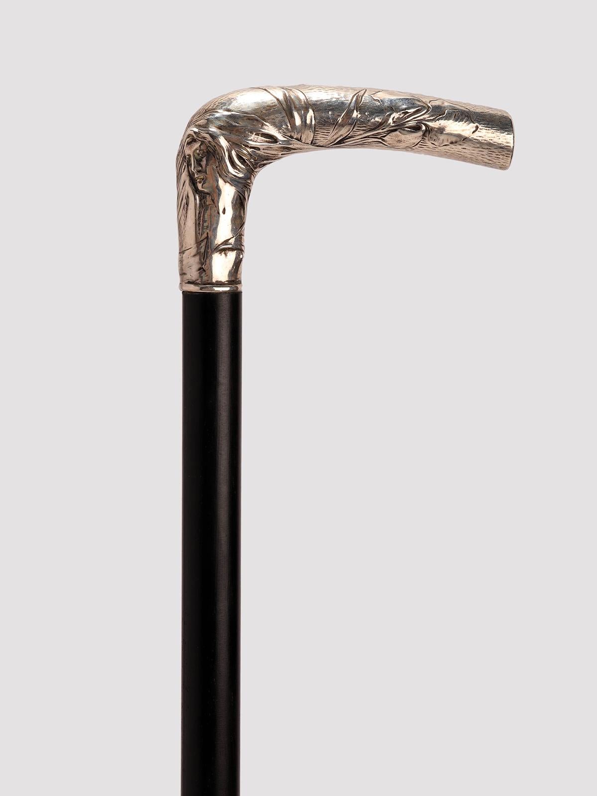 Art Nouveau walking stick. The L-shaped 800 silver knob is embossed and chiselled and depicts the face of a woman with long loose hair and two Iris flowers. Ebony wood barrel. Metal tip. France circa 1900.