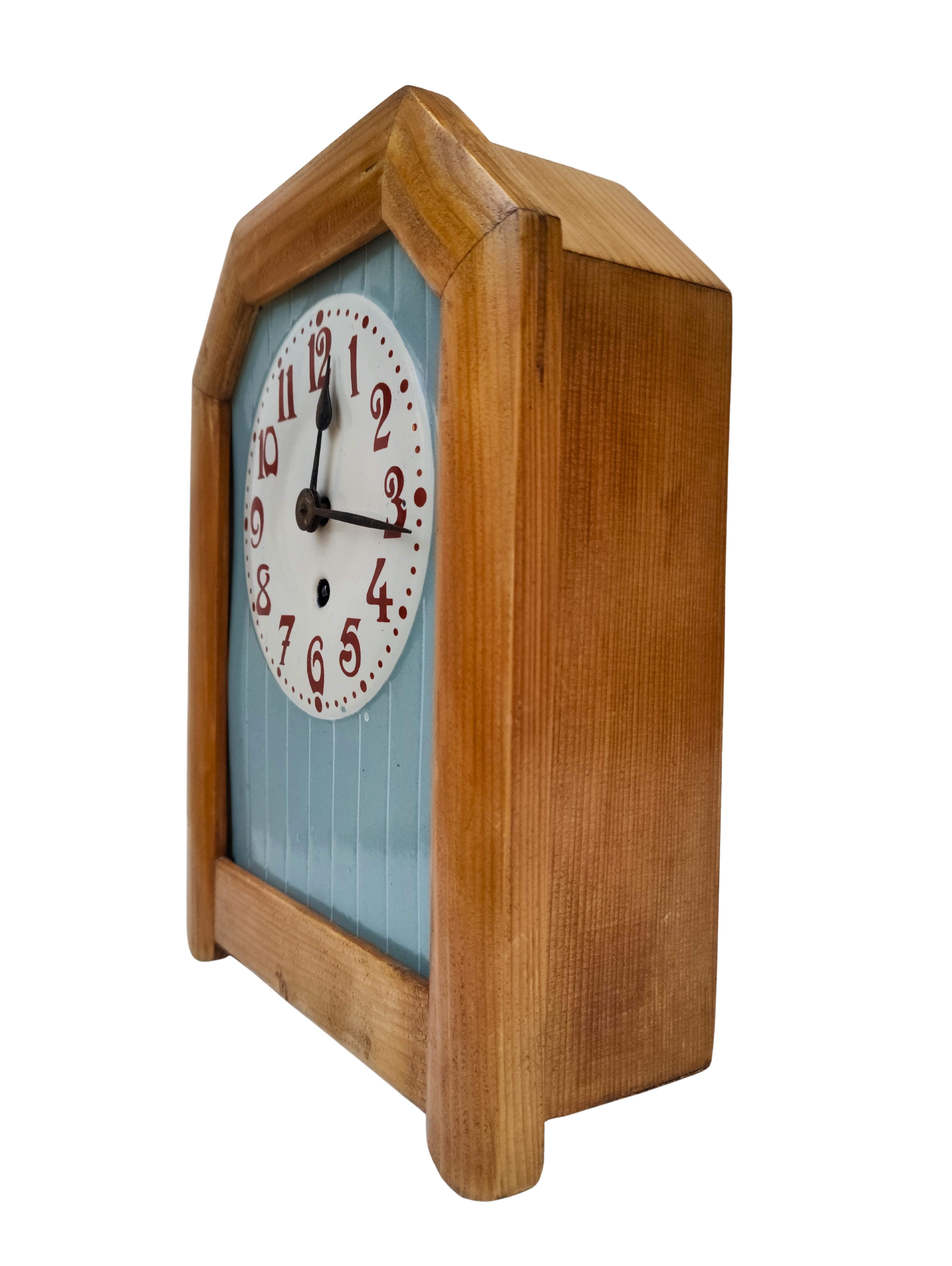 This Art Nouveau wall clock dates to the early 20th century, circa 1905, and is a fine example of restrained Jugendstil design. The clock features a ceramic dial with clearly legible Arabic numerals in a warm red tone, framed by a softly colored