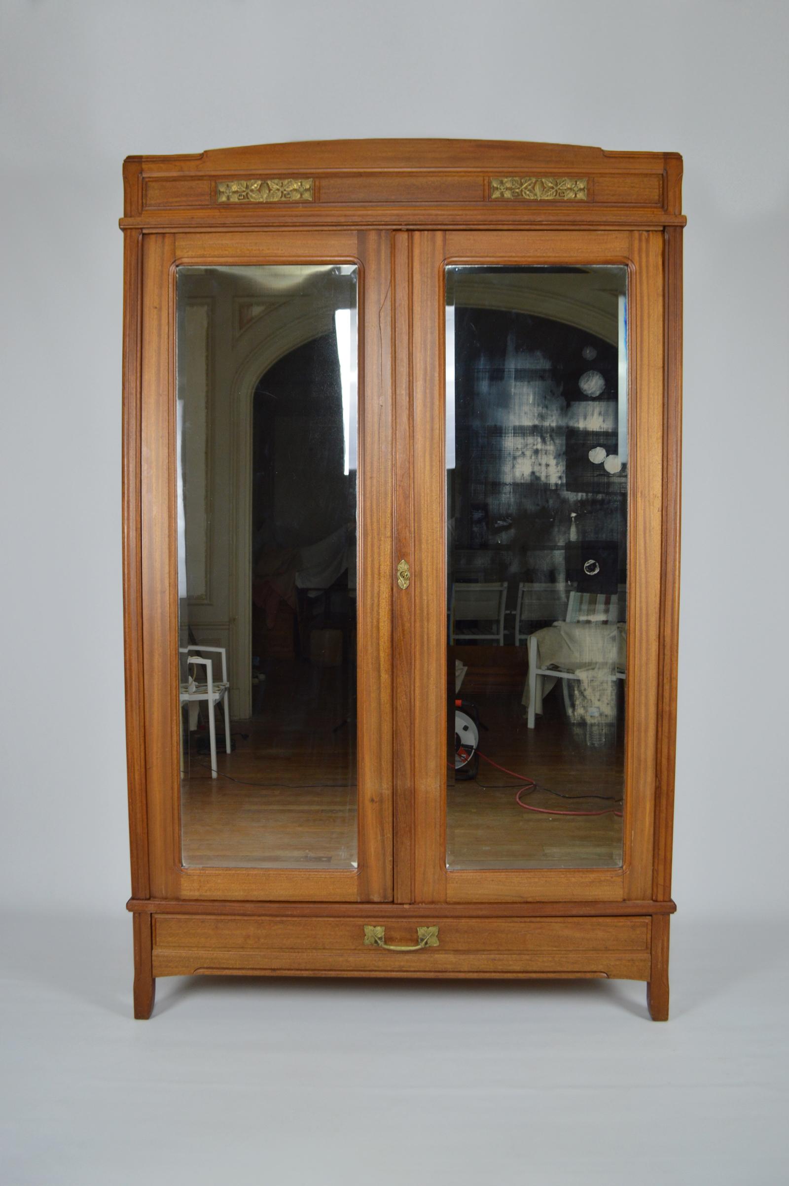 Large double-door mahogany wardrobe / cabinet with beveled mirrors.
On the outside we find a large drawer and a pediment enhanced with beautiful decorative bronzes.
The interior consists of 4 shelves and 2 small drawers.

All the bronze elements