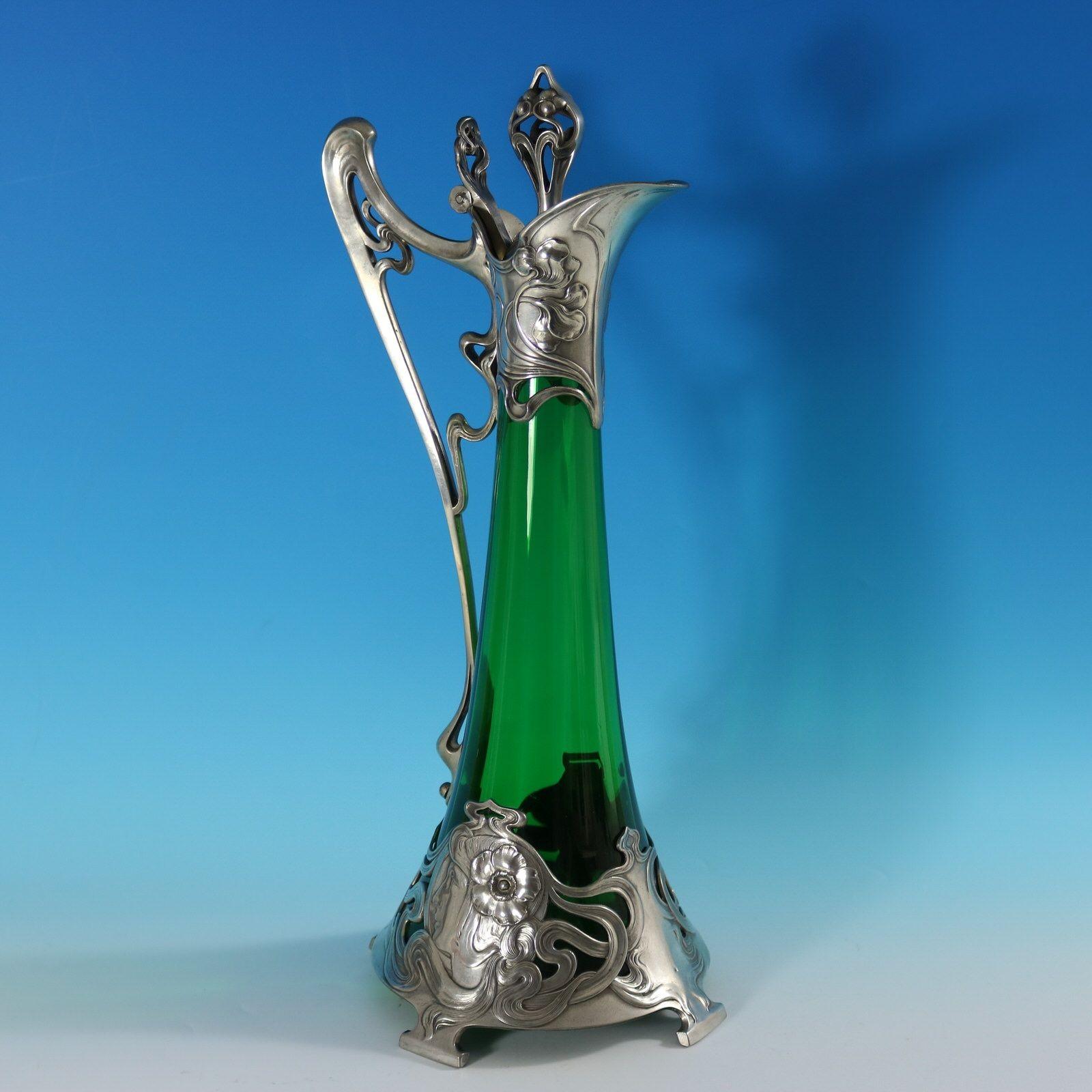 WMF green glass claret jug of typical Art Nouveau stylised form. The bottom mount depictis a maiden's head with a flower in her hair. The hair flows around the piece creating a winding pattern. The upper mount has floral motifs. The finial modelled