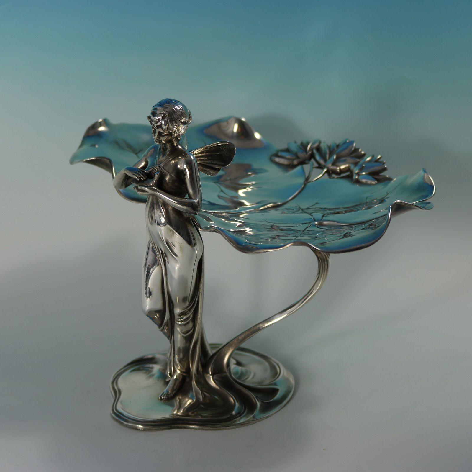 WMF Art Nouveau visiting card tray decorated with a fairy standing before two large lily leaves, holding a dove in her hands. Impressed maker's marks including the WMF in a square mark, 'I/O' ', and '246' to the underside. Illustrated on page 167,