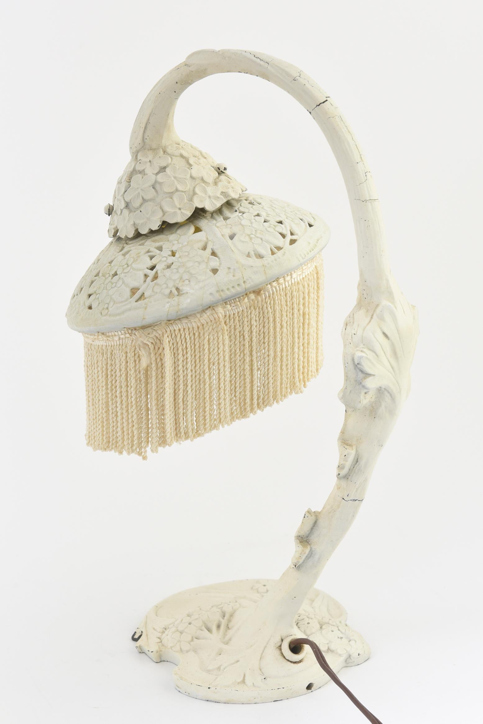 Art Nouveau white arched lamp on base with flowers and leaves leading up to a woman’s profile with flowing hair and a pierced floral shade. White fringe has been later applied and can be easily removed. U.S. wired and working; takes a candelabra