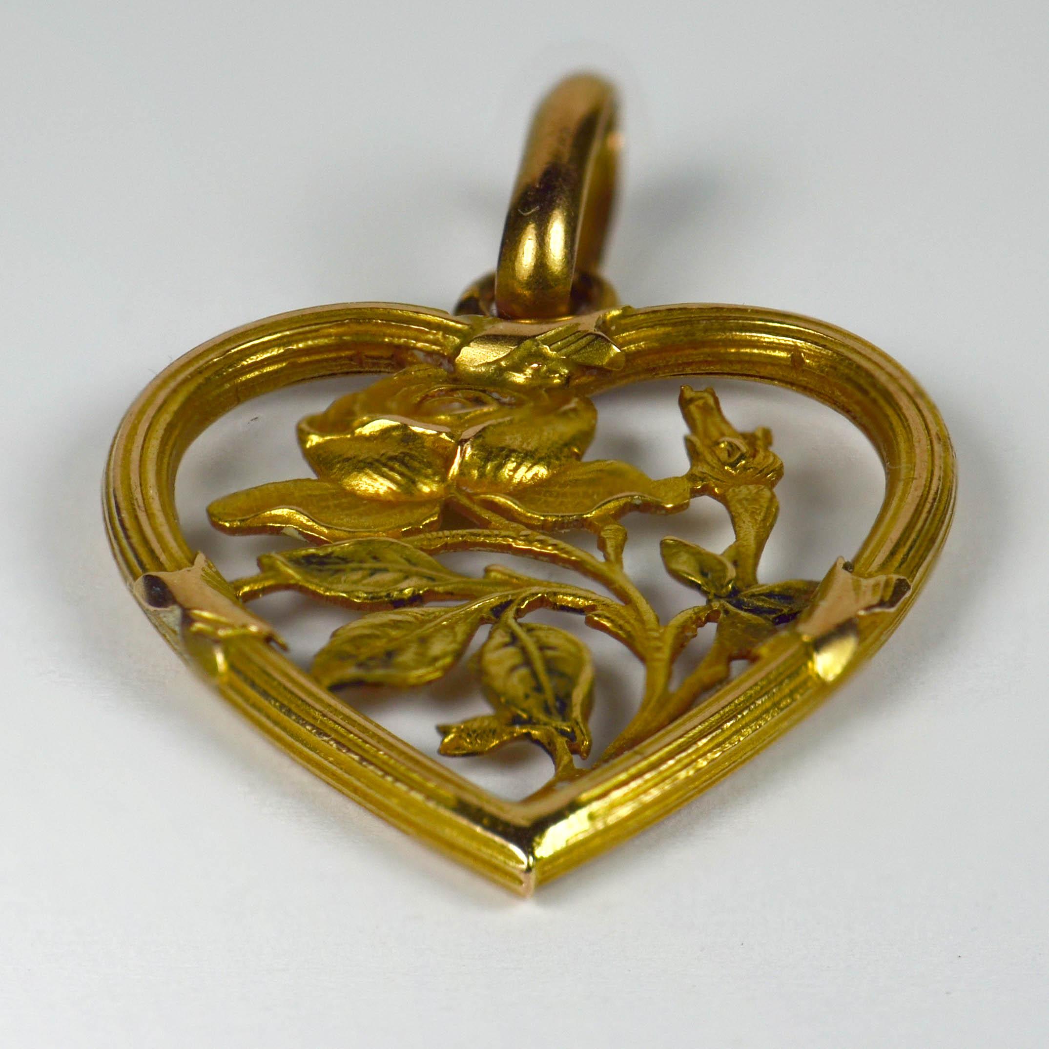 An Art Nouveau charm or pendant in 18 karat yellow gold designed as a reeded heart shaped frame bound with crosses of ribbon, enclosing a rose in full bloom with a secondary rosebud. Stamped with the eagle's head for French manufacture and 18 karat