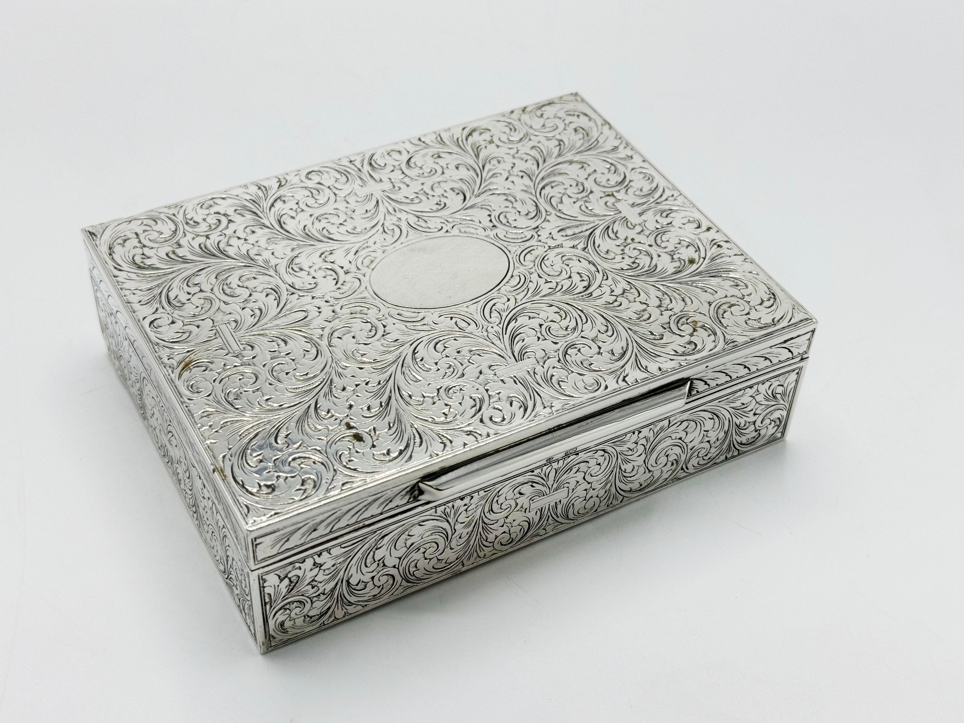 Art Noveade 800 German Silver Jewelry Box
A Box with an intricate pattern engraved on its surface. The pattern consists of swirls and floral designs that cover the entire top and sides of the box. There is a plain, unadorned oval space in the center