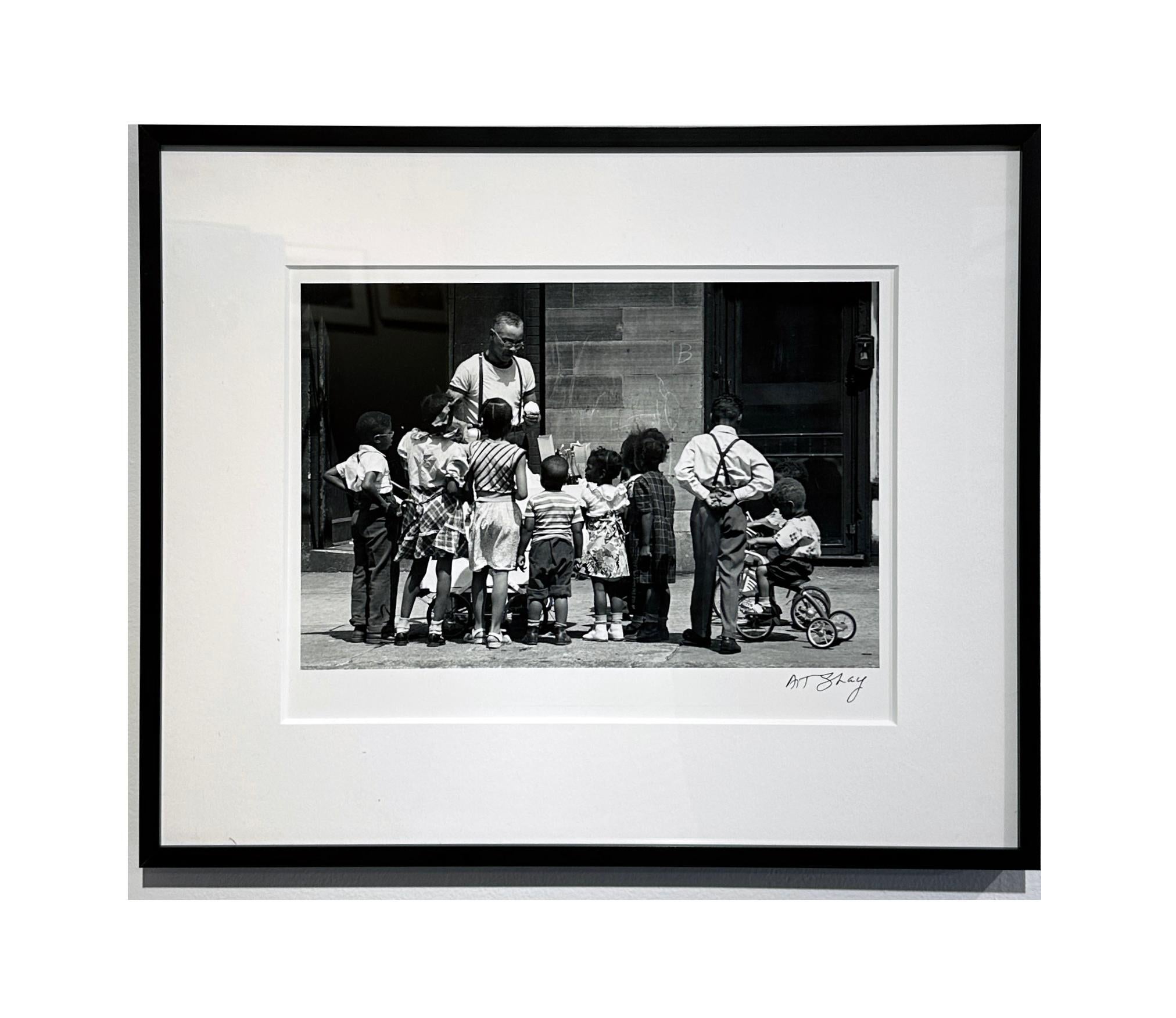 In diesem wunderbaren Beispiel für Art Shays meisterhafte Straßenfotografie versammeln sich Kinder mit geballter Aufmerksamkeit um den Eisverkäufer.  CIRCA 1949, dieses Foto fängt die Unschuld vergangener Tage ein.  Es ist mattiert und gerahmt in
