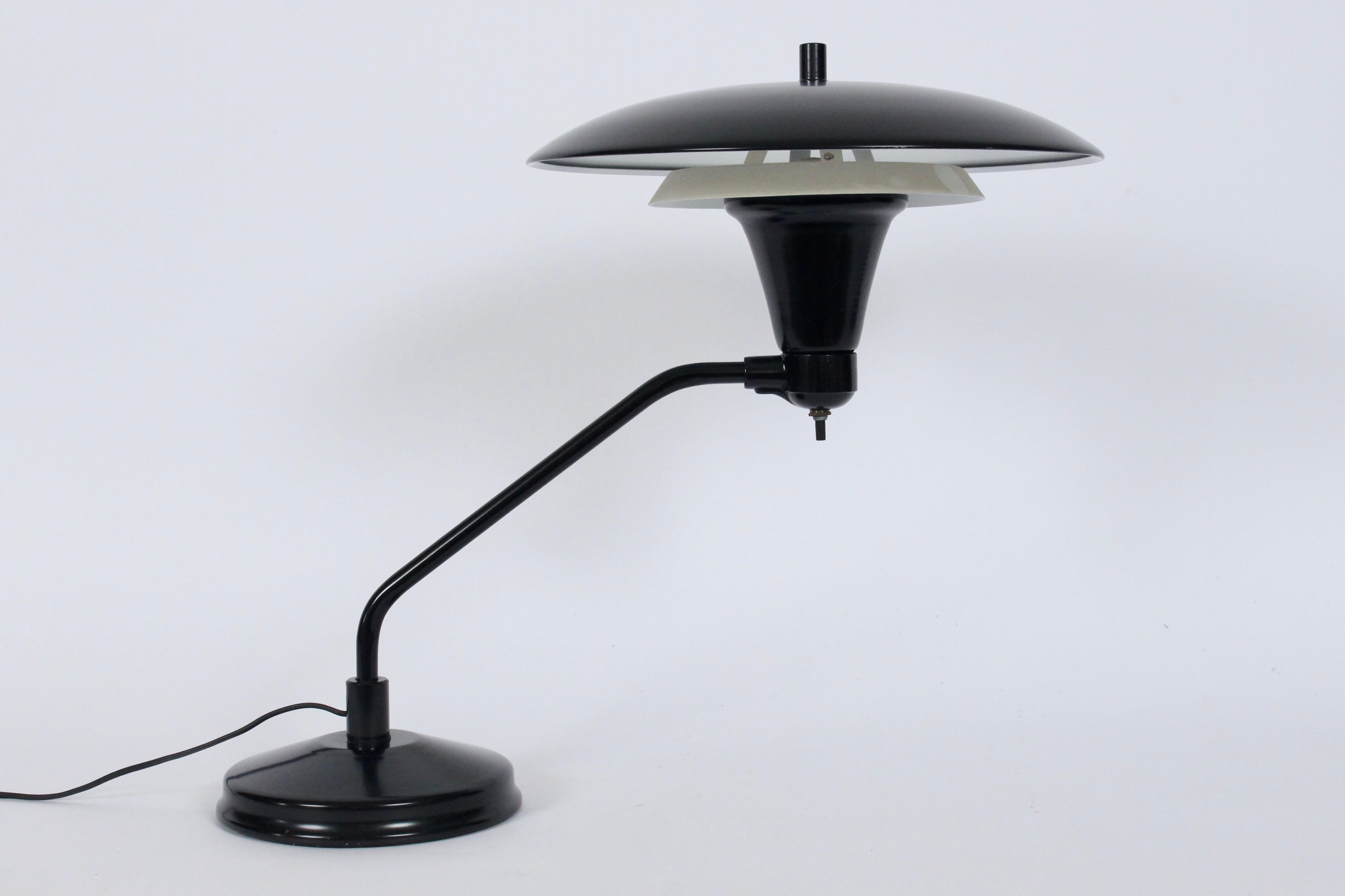 Art Specialty Co two tier black and white enamel desk lamp. Featuring a double tiered circular Shade, cantilevered arm, White enamel interior, on heavy round base. Standard socket. Wide reflective light field. Shade 13D. Base 7D. Extra fine original