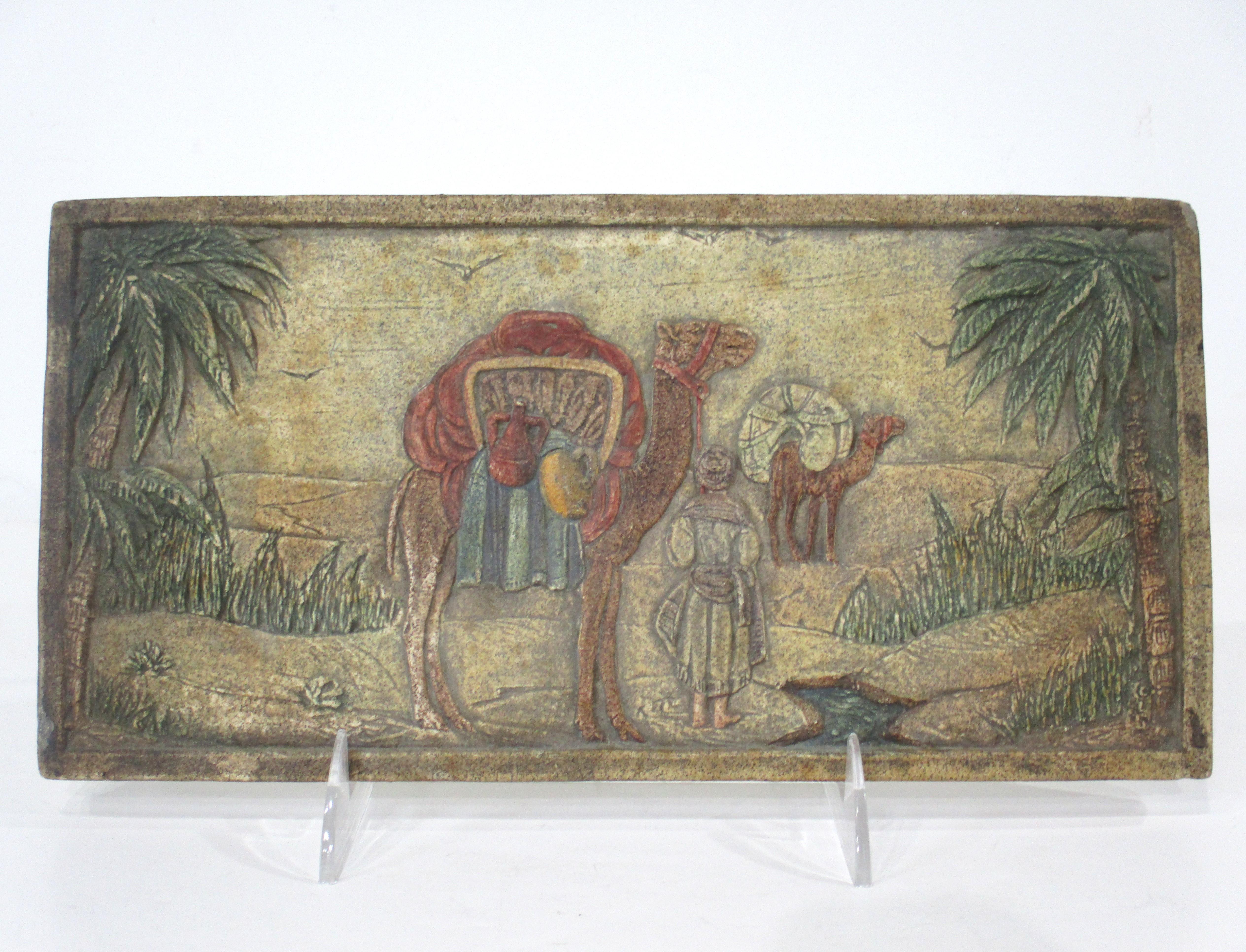 A larger sized Arts and Crafts hearth art tile depicting a scenic view of a desert with travelers on camels . Hand colored and crafted by the California Art Tile Company , Richmond California . Incised to the verso with the style number and maker