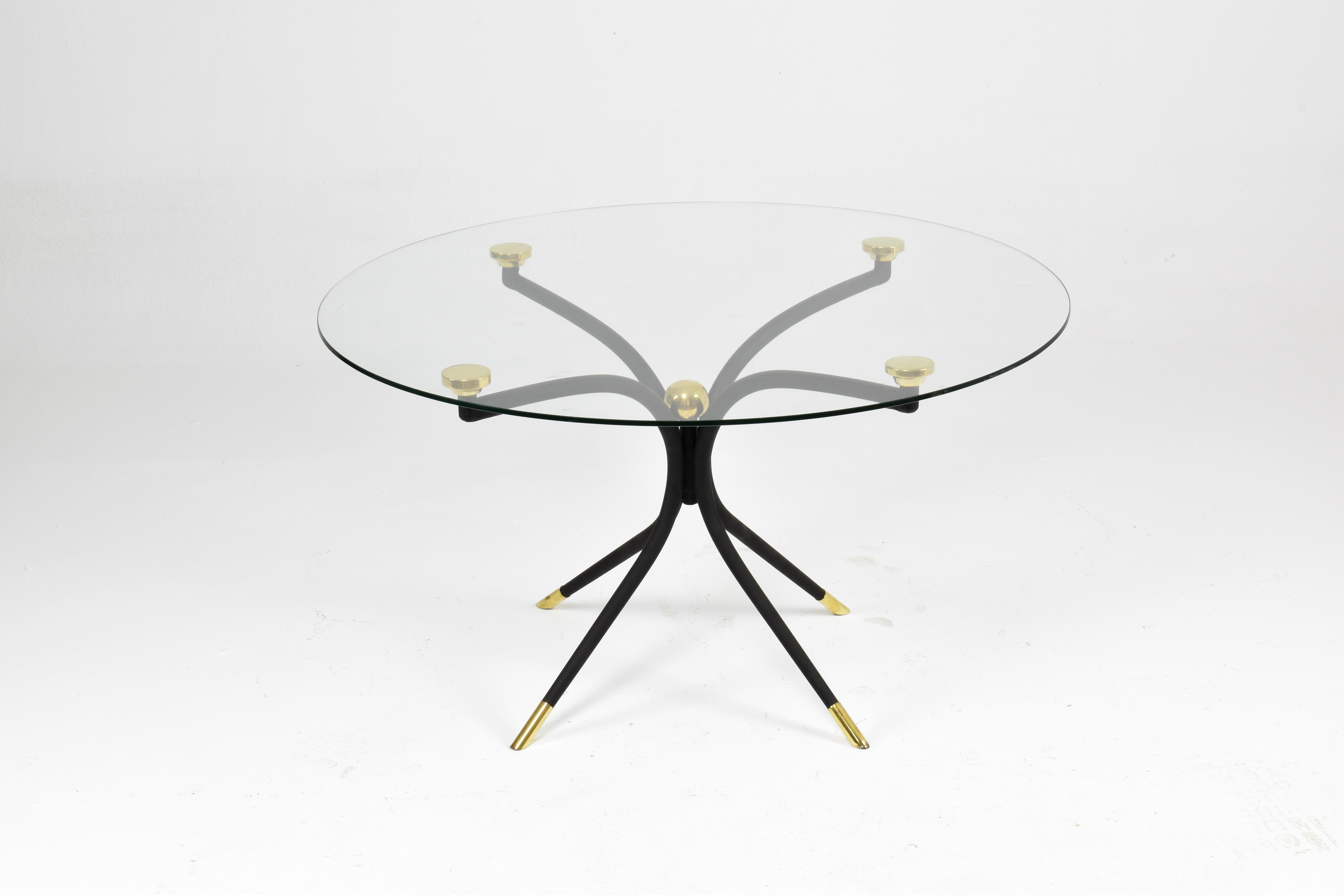 The Arte table plays with tension and harmony—its four-legged base curves upward like calligraphic strokes, supporting a round glass top in a barely-there balance. Crafted in painted iron with polished brass accents, it’s a sculptural take on the