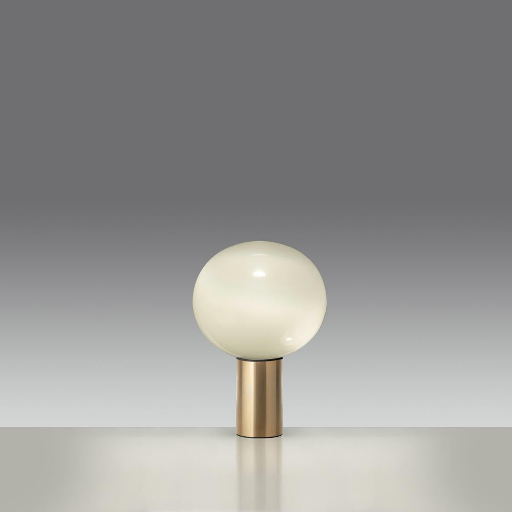 Now available in stunning gold, Laguna table is a spherical table lamp with raised base provides a softly diffused light on the tabletop and casts a warm light in its surrounding environment. 
This modern and elegant table features handblown glass