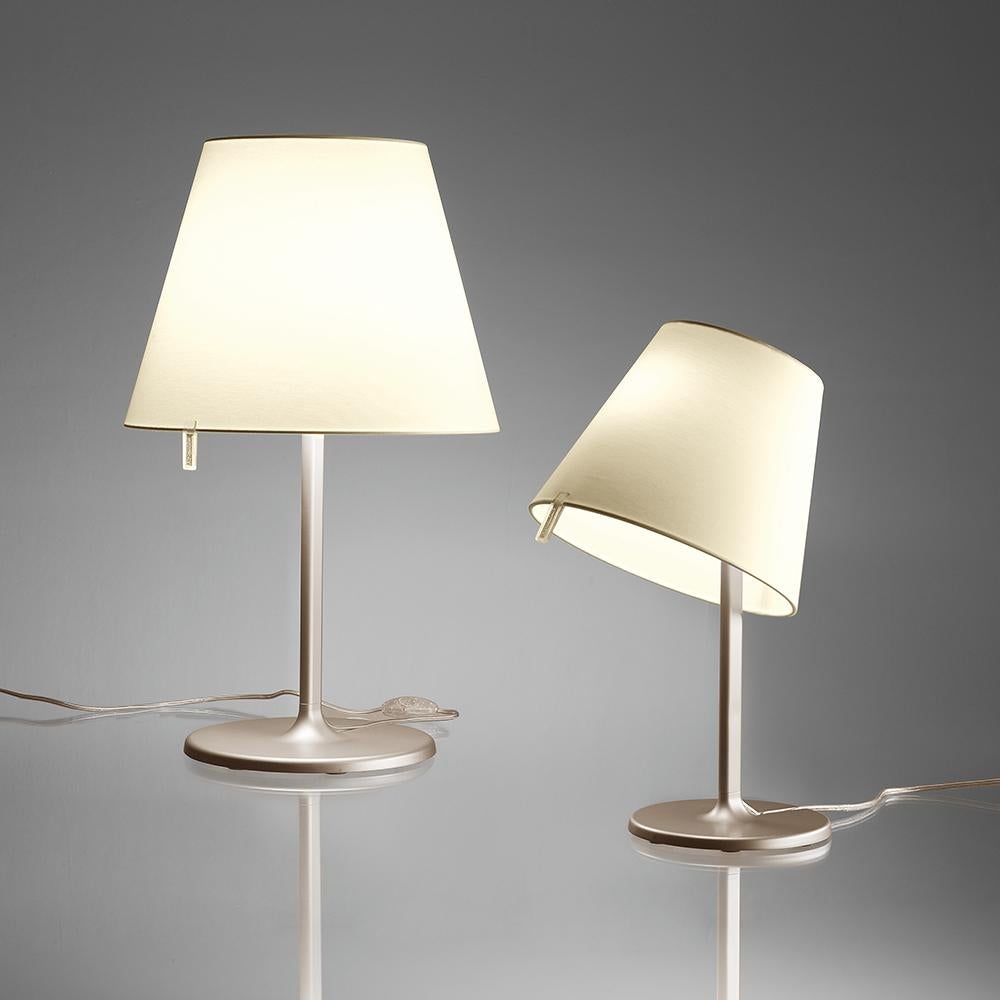 A silk satin fabric shade connected to a painted zamac base via a painted aluminum stem, Melampo can be adjusted for direct and indirect light. 

Mini accommodates two shade positions while the standard task lampshade can be maneuvered into three