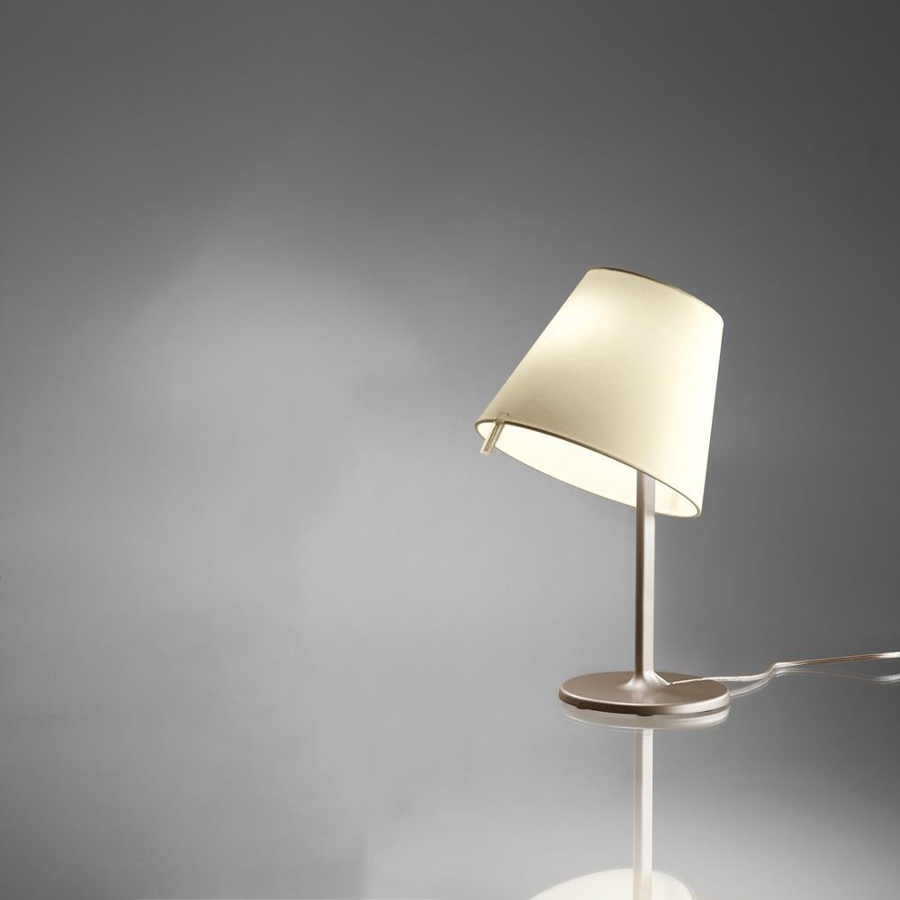 A silk satin fabric shade connected to a painted zamac base via a painted aluminium stem, Melampo can be adjusted for direct and indirect light. 

Mini accommodates two shade positions while the standard task lamp shade can be maneuvered into three