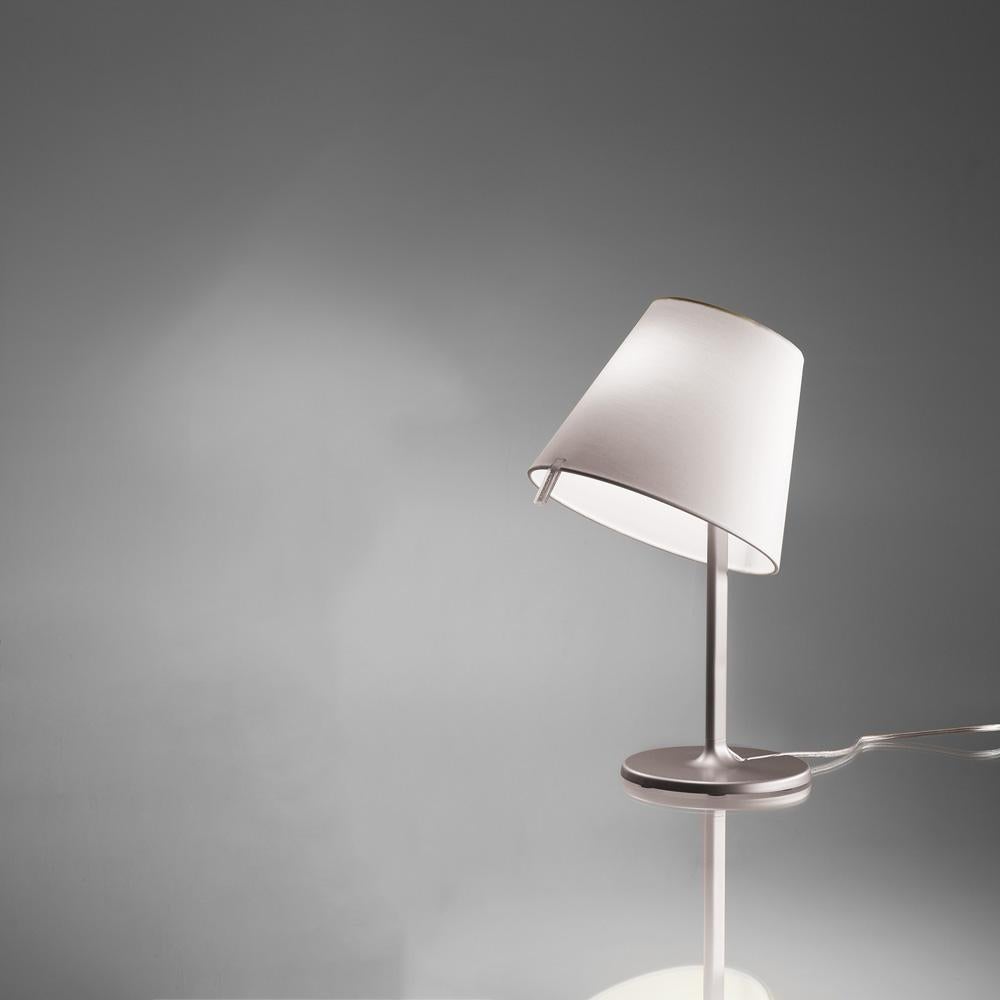 A silk satin fabric shade connected to a painted zamac base via a painted aluminum stem, Melampo can be adjusted for direct and indirect light. 

Mini accommodates 2 shade positions while the standard task lamp shade can be maneuvered into 3