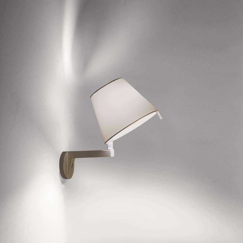 A silk satin fabric shade connected to a painted white zamac base via a painted aluminum stem, Melampo mini can be adjusted for direct and indirect light. 

Melampo Mini accommodates two positions while the standard task lamp can be maneuvered into