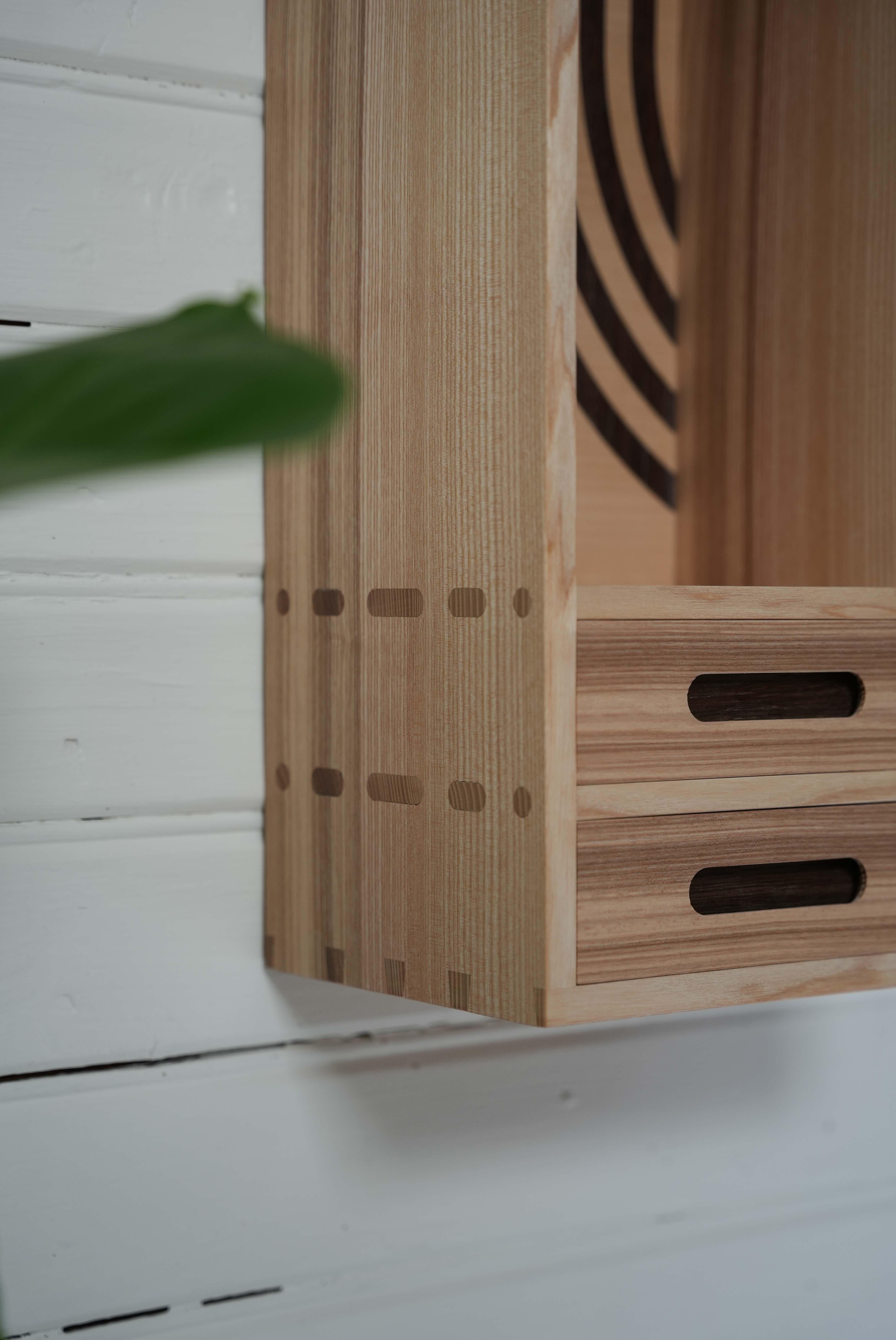 Este armario de pared está hecho a mano con fresno sueco y roble ahumado, tratados con aceite de cera dura para resaltar la belleza natural de la madera y darle un acabado suave y duradero. La carpintería incluye colas de milano y juntas de mortaja