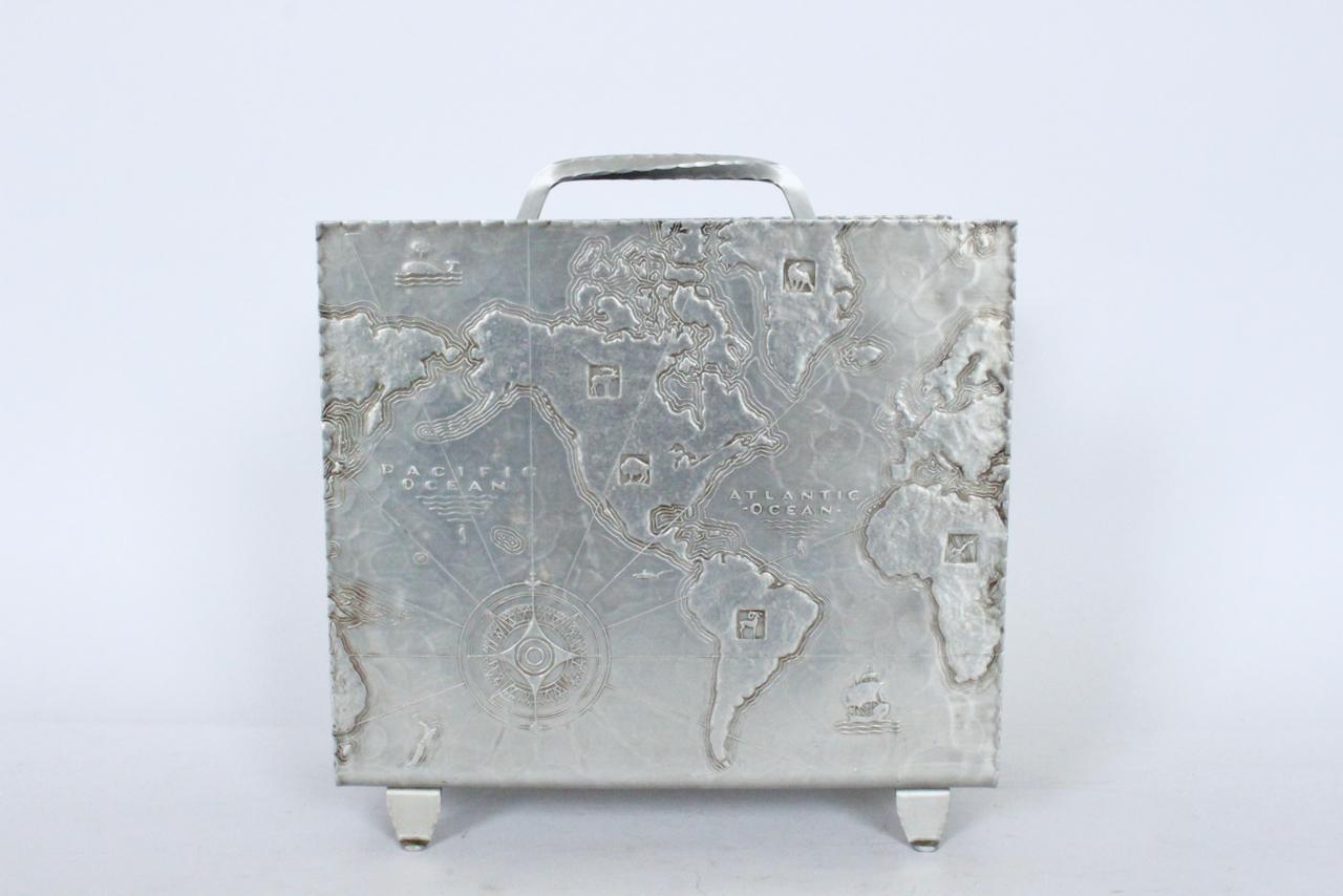 Art Deco Arthur Armour Hammered aluminum World map magazine rack, 1930s Featuring a smooth handled hand wrought hammered aluminum rectangular form, scalloped rim, low profile world map, a top a footed base. Handle forms divided interior area.