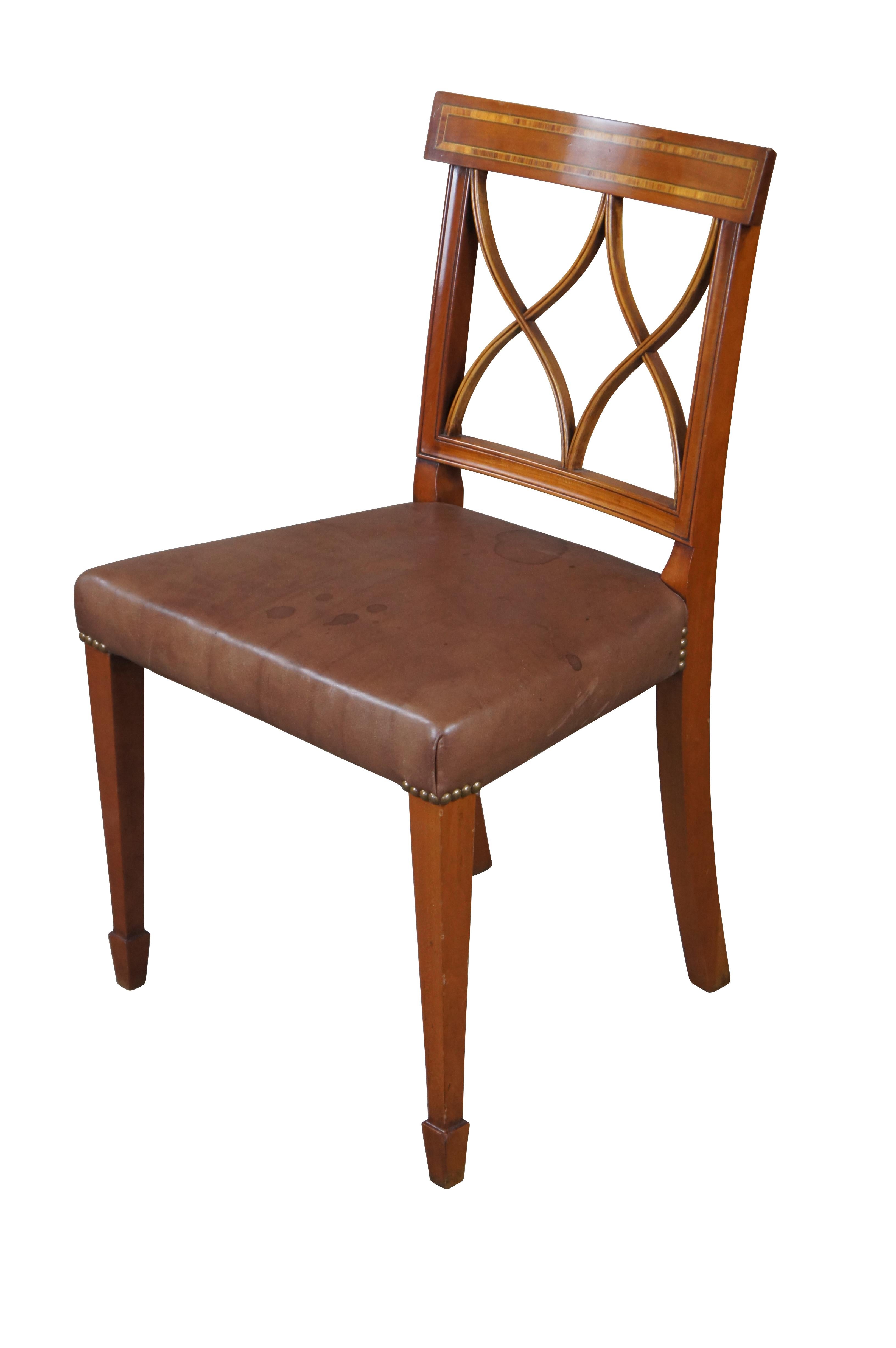 Sedia da pranzo in pelle intarsiata in stile Sheraton inglese di Arthur Brett.  Presenta un profilo curvo con bordatura trasversale su uno schienale intarsiato a doppia X traforata che conduce a una seduta in pelle marrone.  La pelle è accentuata da