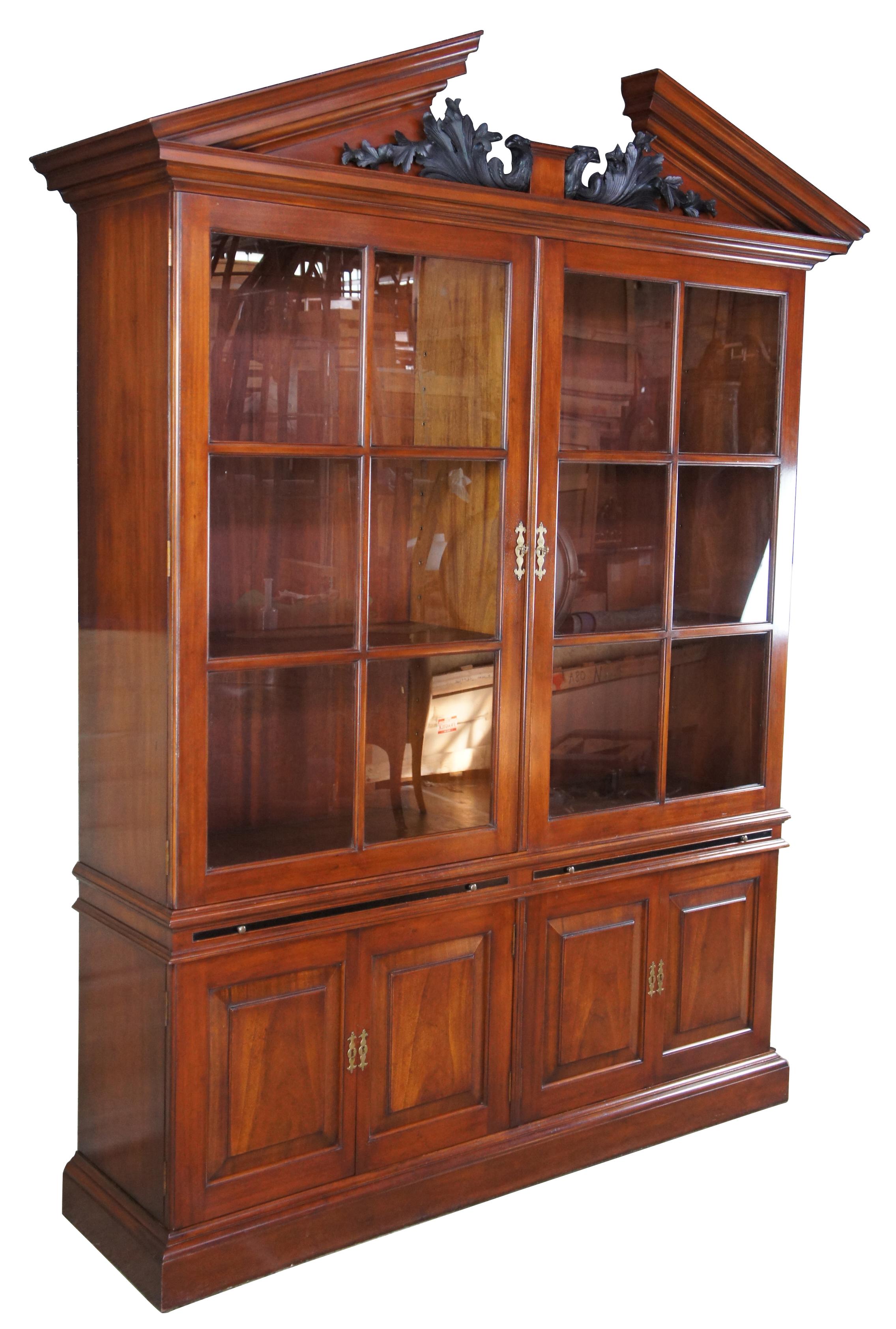 Late 20th century George II style library bookcase by Arthur Brett. Made from mahogany with a wide base featuring two six pained doors opening to adjustable shelves over pullout work surfaces and lower cabinet storage. Includes an open pediment top