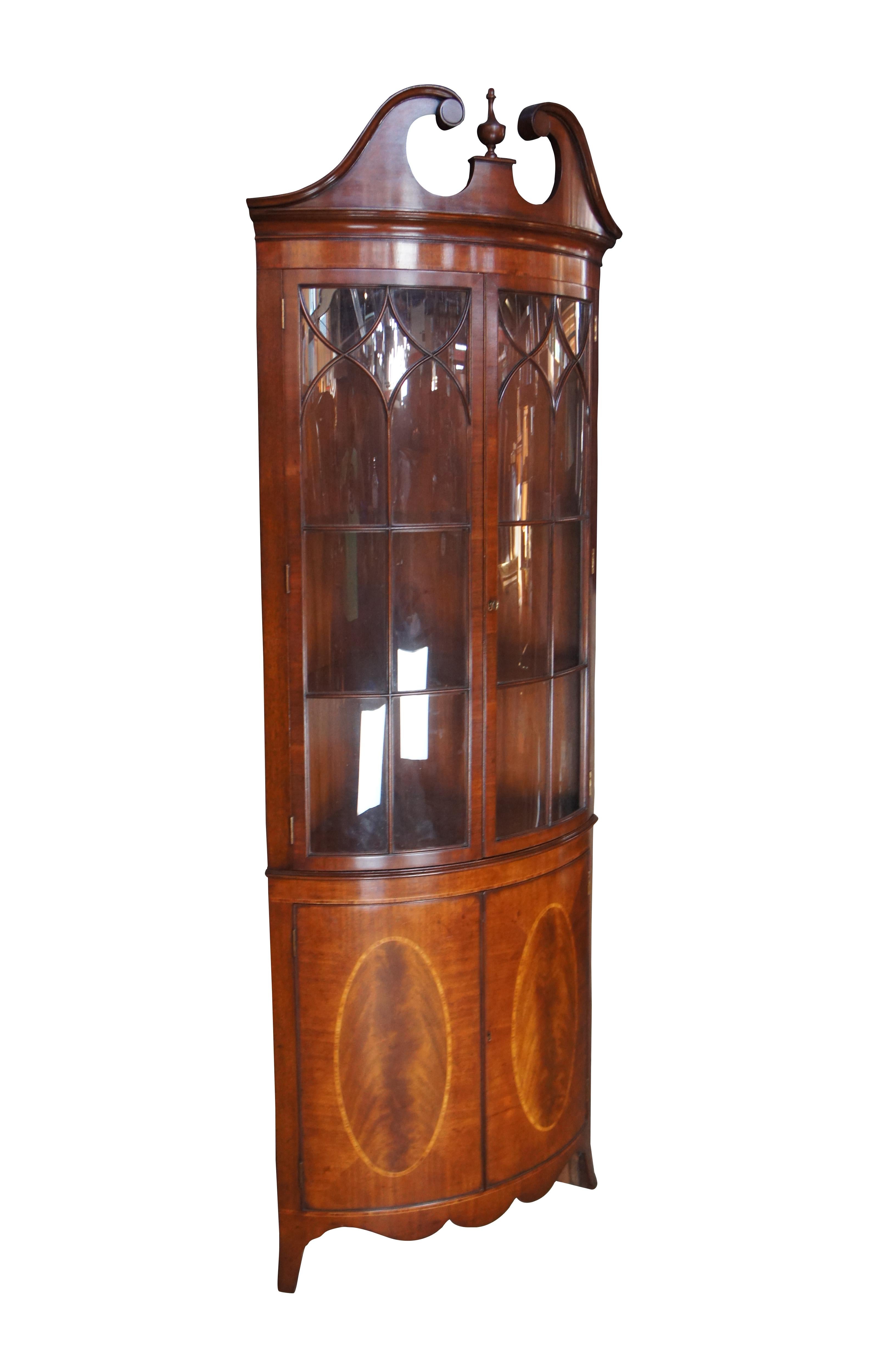 A petite English corner cabinet by Arthur Brett, circa 1980s. Features a curved form made from mahogany with a tall glass covered hutch, having ornate fretwork and two interior shelves. The base showcases two lower doors with crossbanded crotch