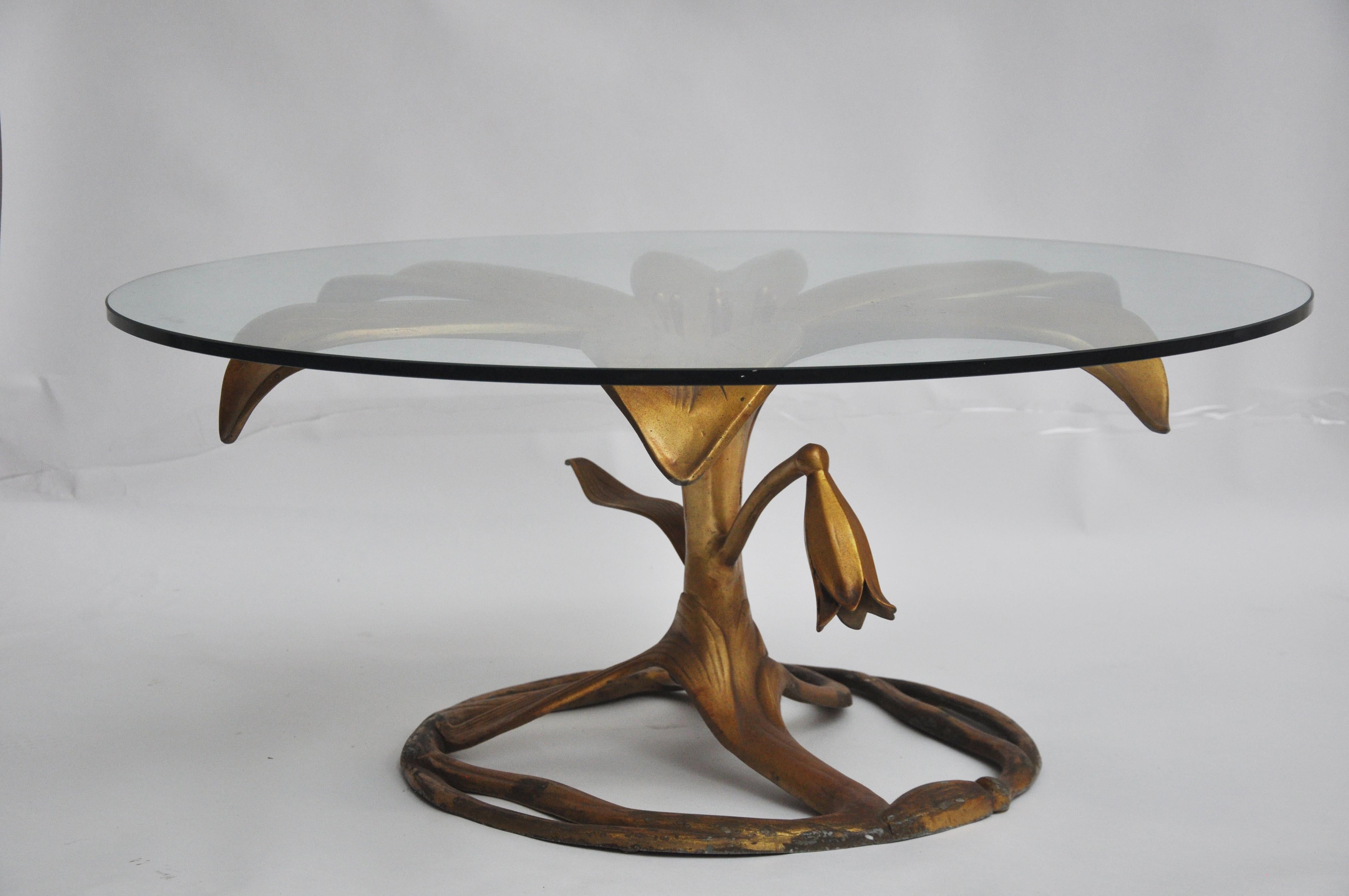 The coffee table is made out of aluminum and painted in gold. There is a large glass round top. There is some patina on the metal base.
