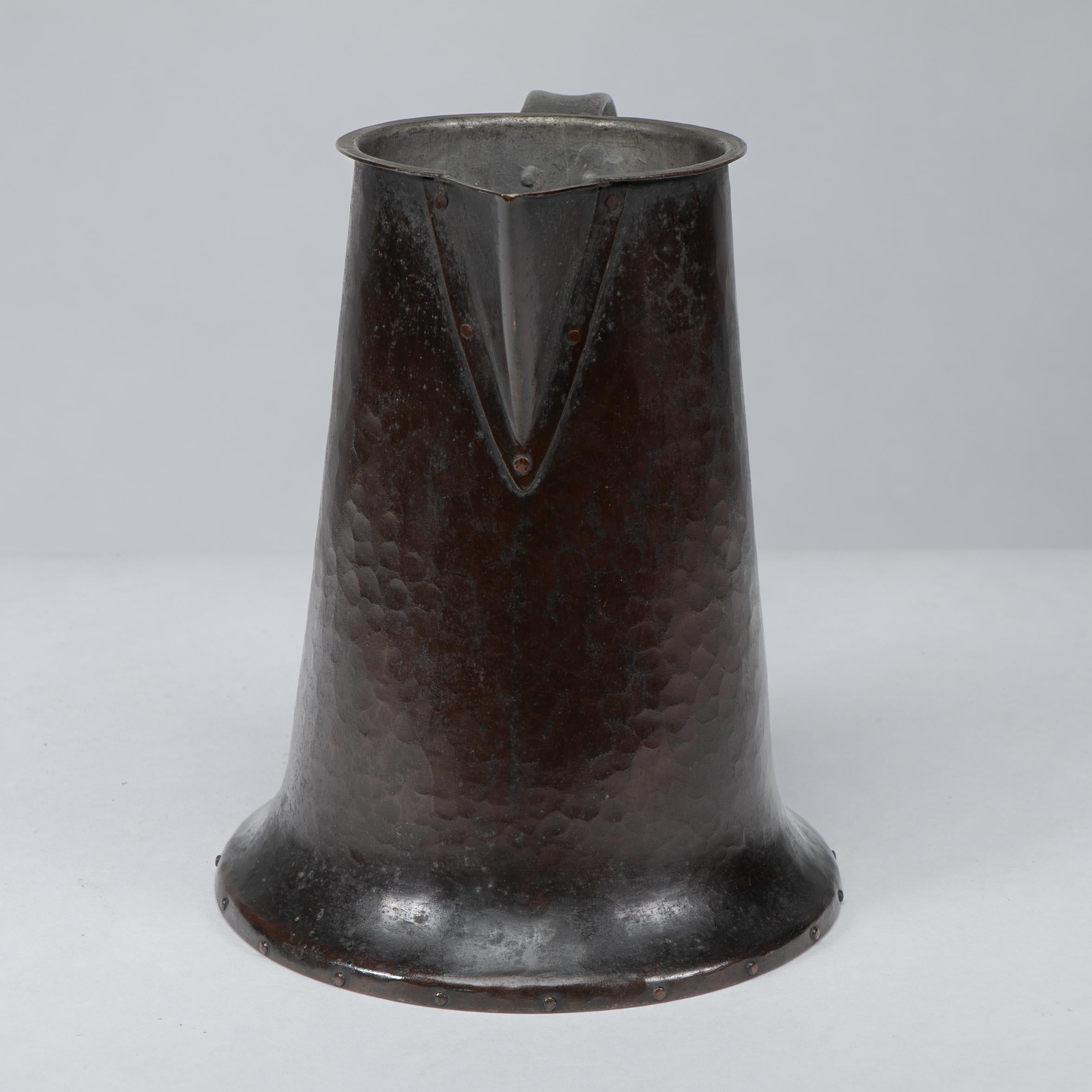 Arthur Stansfield Dixon entwarf für die Guild of Handicraft in Birmingham. Ein handgehämmerter Krug mit einem handgeformten Henkel, der am Boden und an der Unterseite des Henkels ein geschliffenes, gespreiztes und genietetes Detail im fließenden