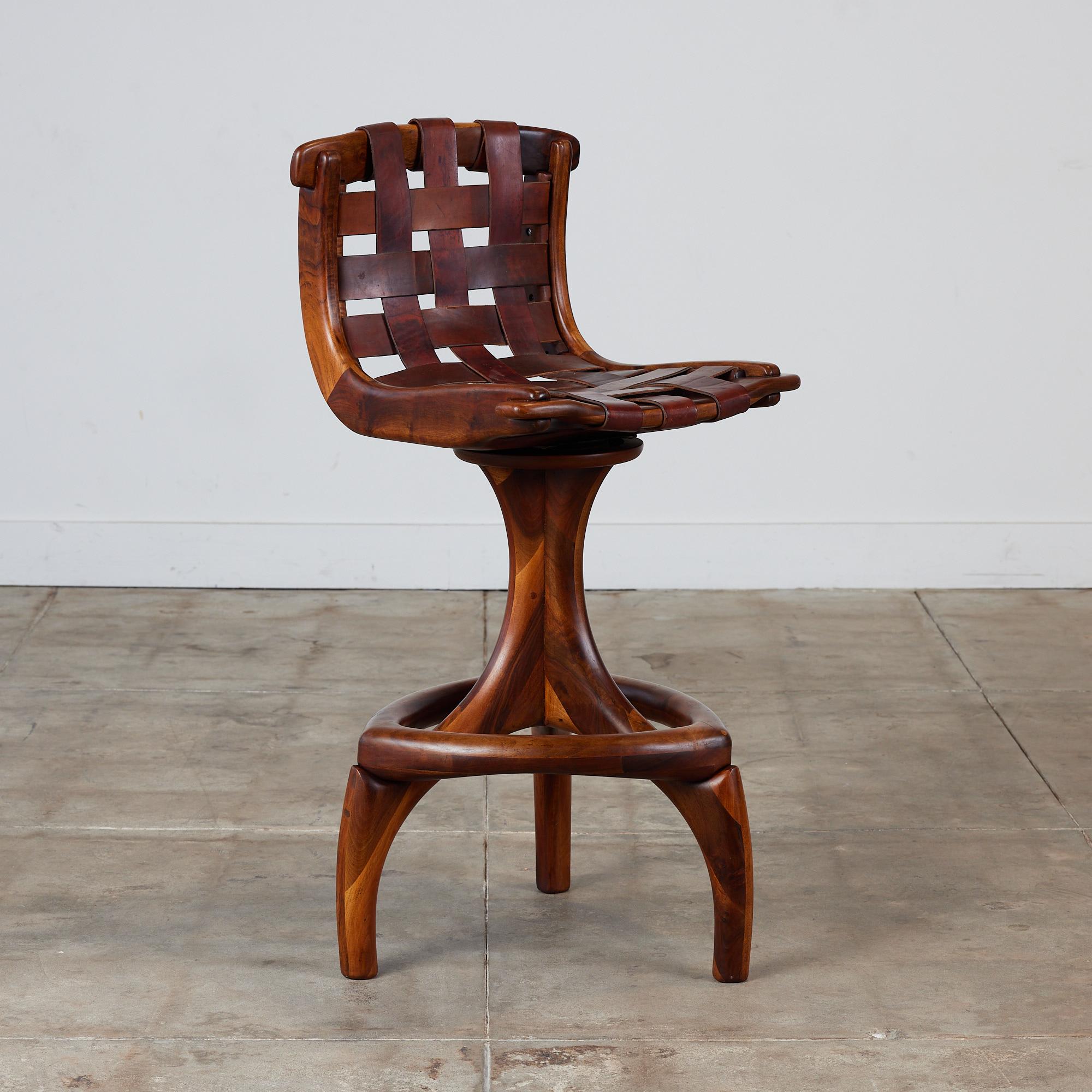Walnut studio craft swivel stool by California designer, Arthur Espenet Carpenter, circa 1970s. The stool features a woven leather slung seat with sculpted wood L-shape frame. The stool has a 360 degree swivel mechanism and is supported by three